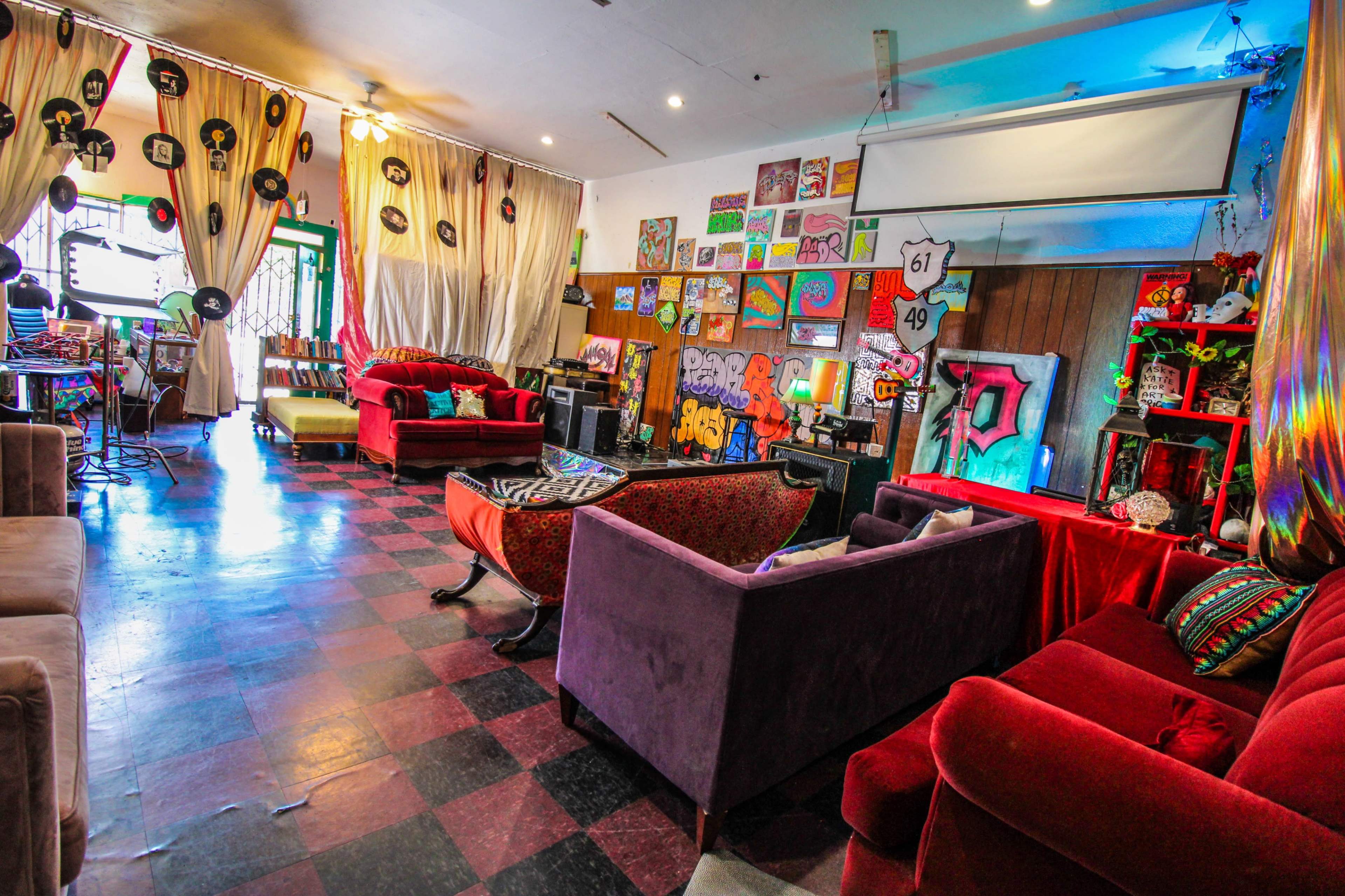 A colorful lounge area with red and purple sofas, decorated walls featuring various artworks, and a large screen on the wall.