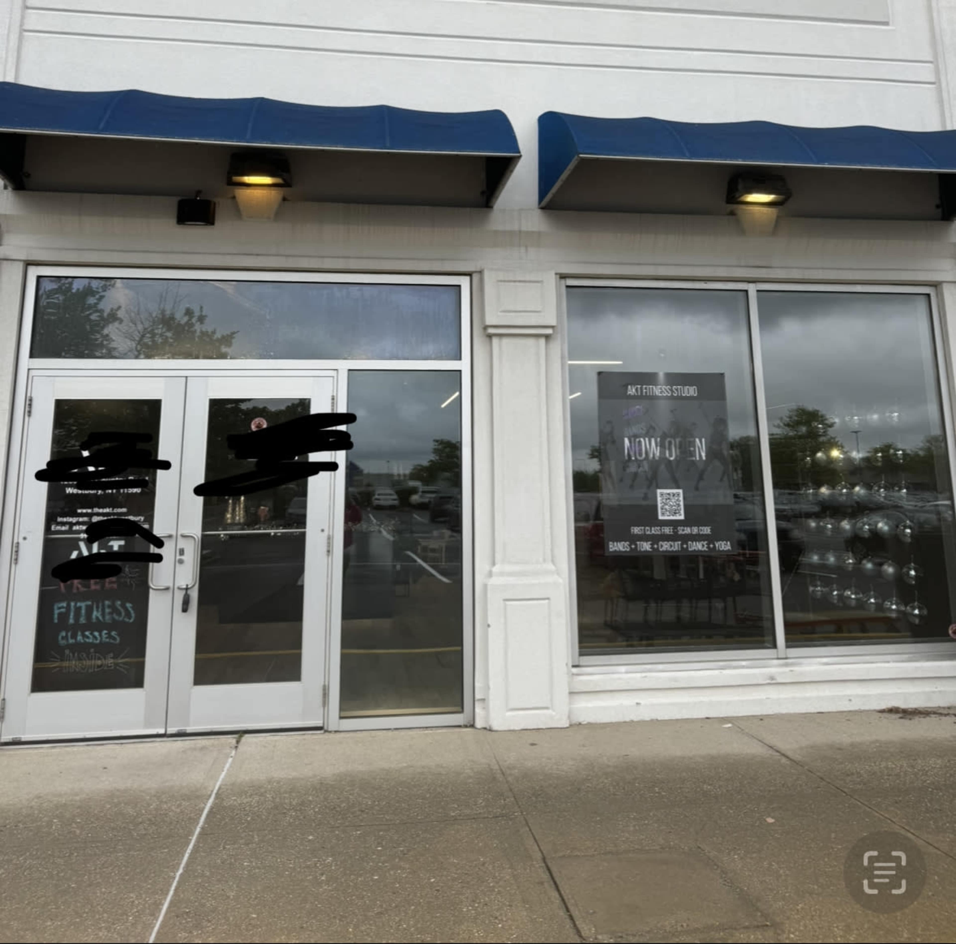 The exterior of a fitness studio with large glass windows and a sign promoting free fitness classes, located in a shopping area.
