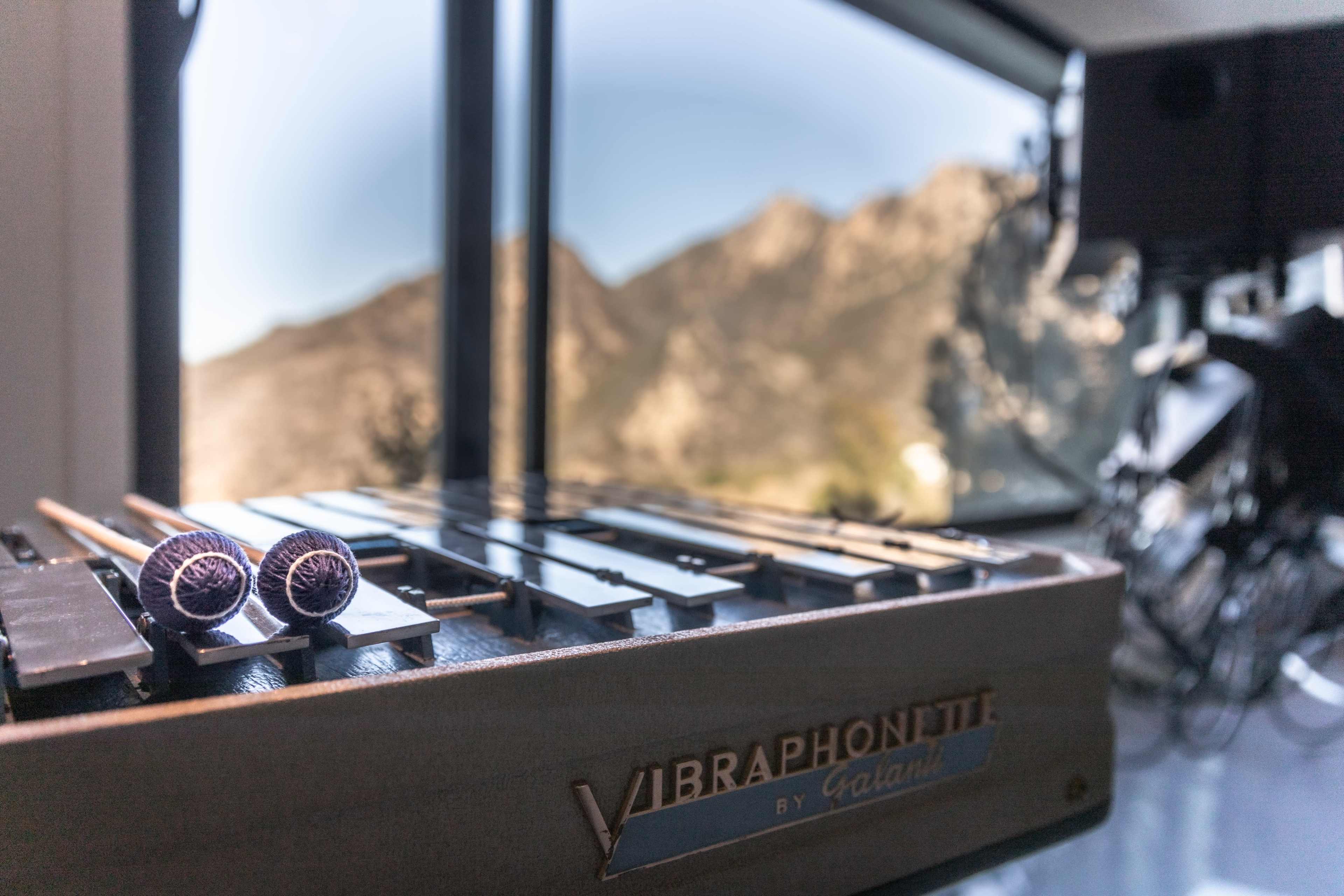 A vibraphone sits in the foreground with mountains visible through a large window in the background.