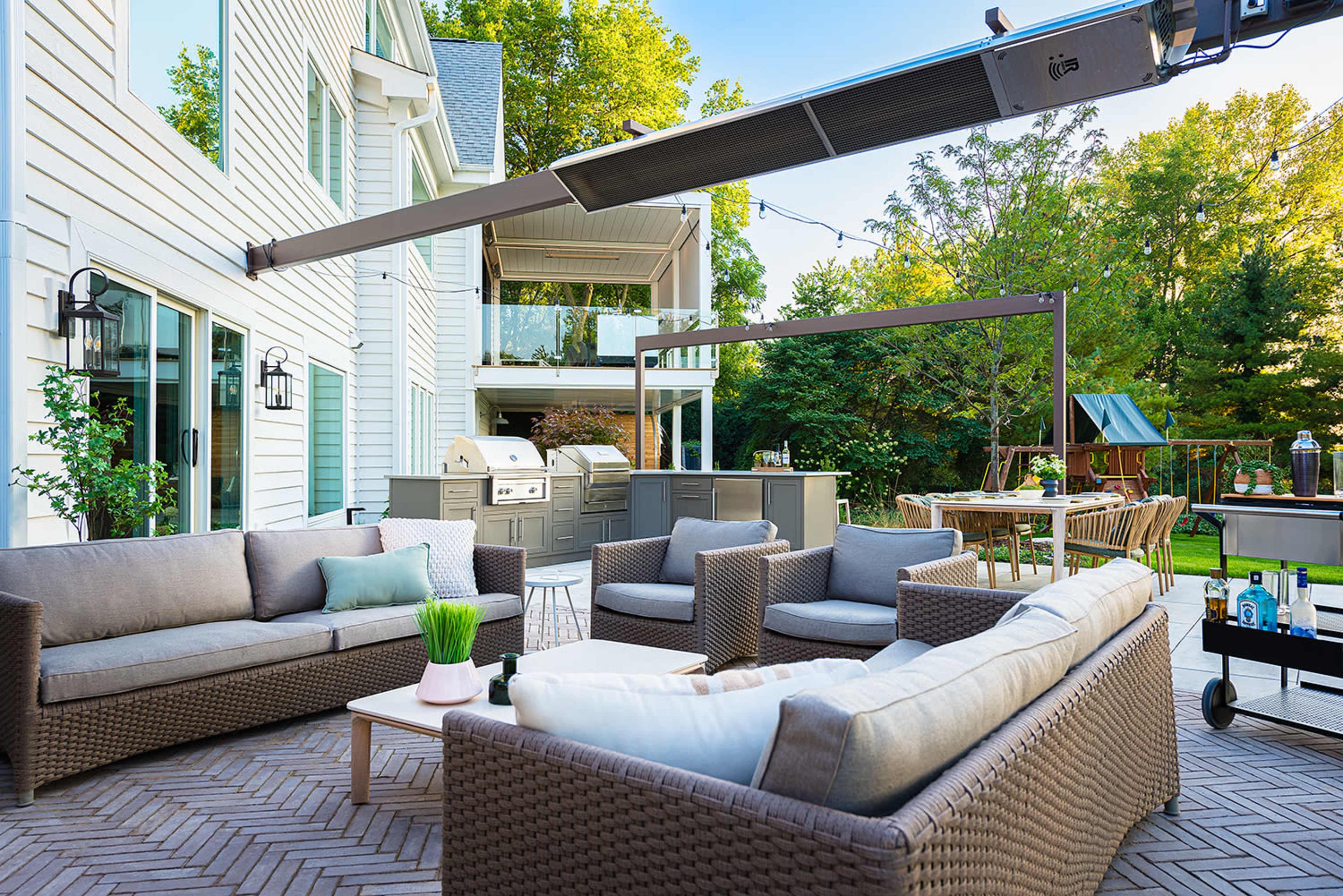 An outdoor patio with wicker furniture, a grill, and a dining area surrounded by greenery.