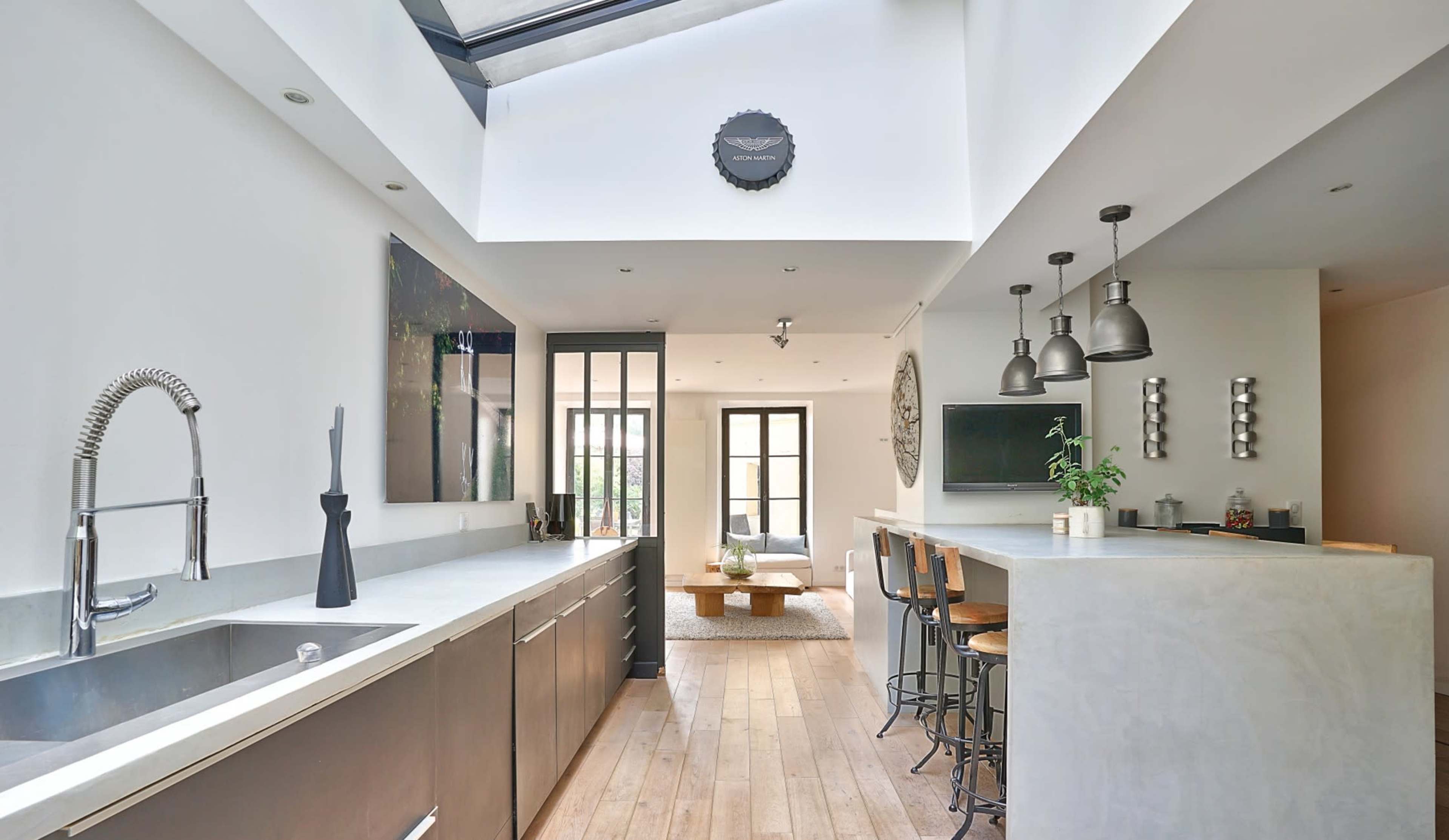 A modern kitchen with a linear design features a central island, sleek cabinetry, and large windows allowing natural light to enter.