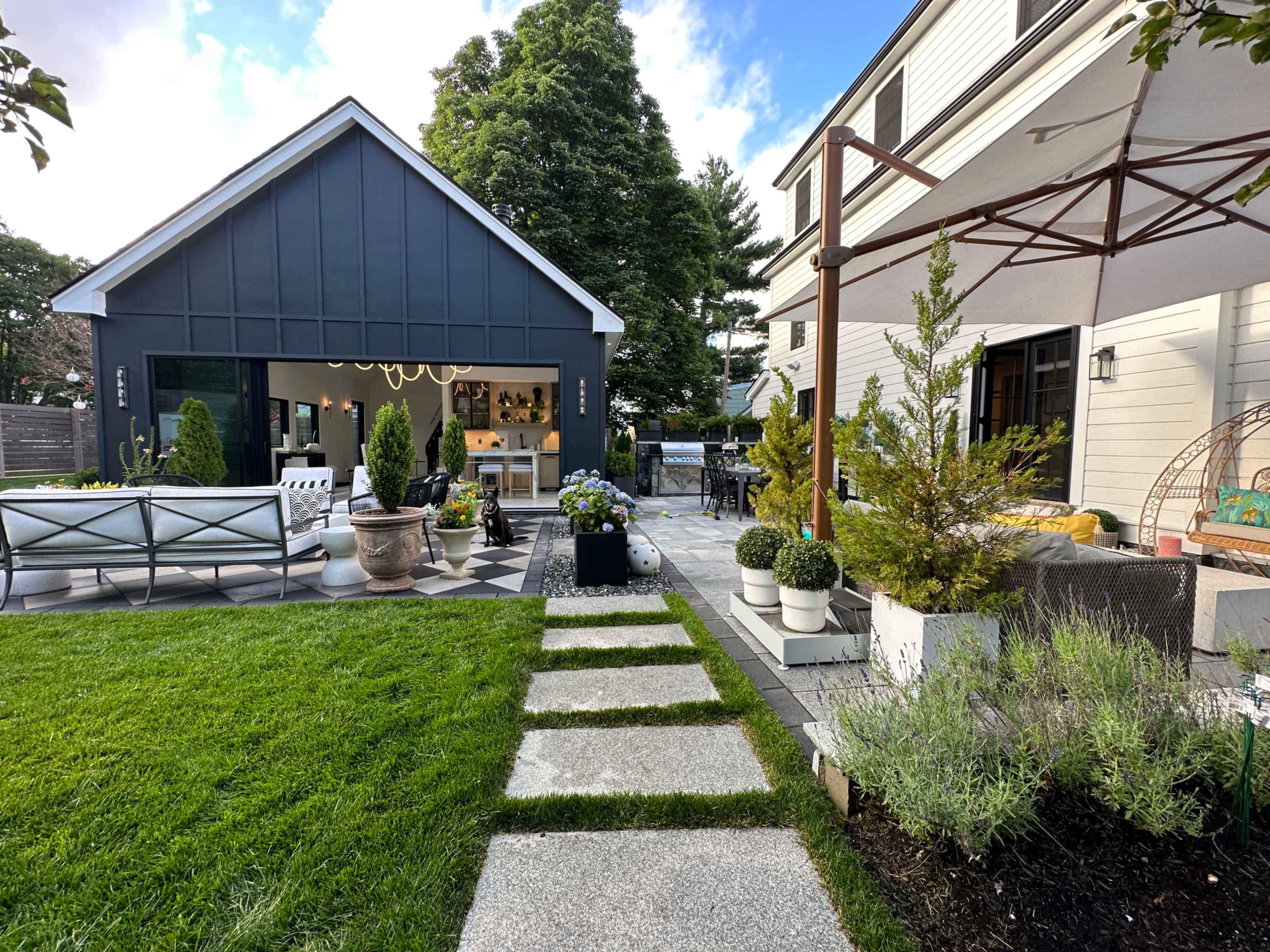 A landscaped backyard featuring a stone pathway leading to a modern shed, surrounded by greenery and outdoor furniture.