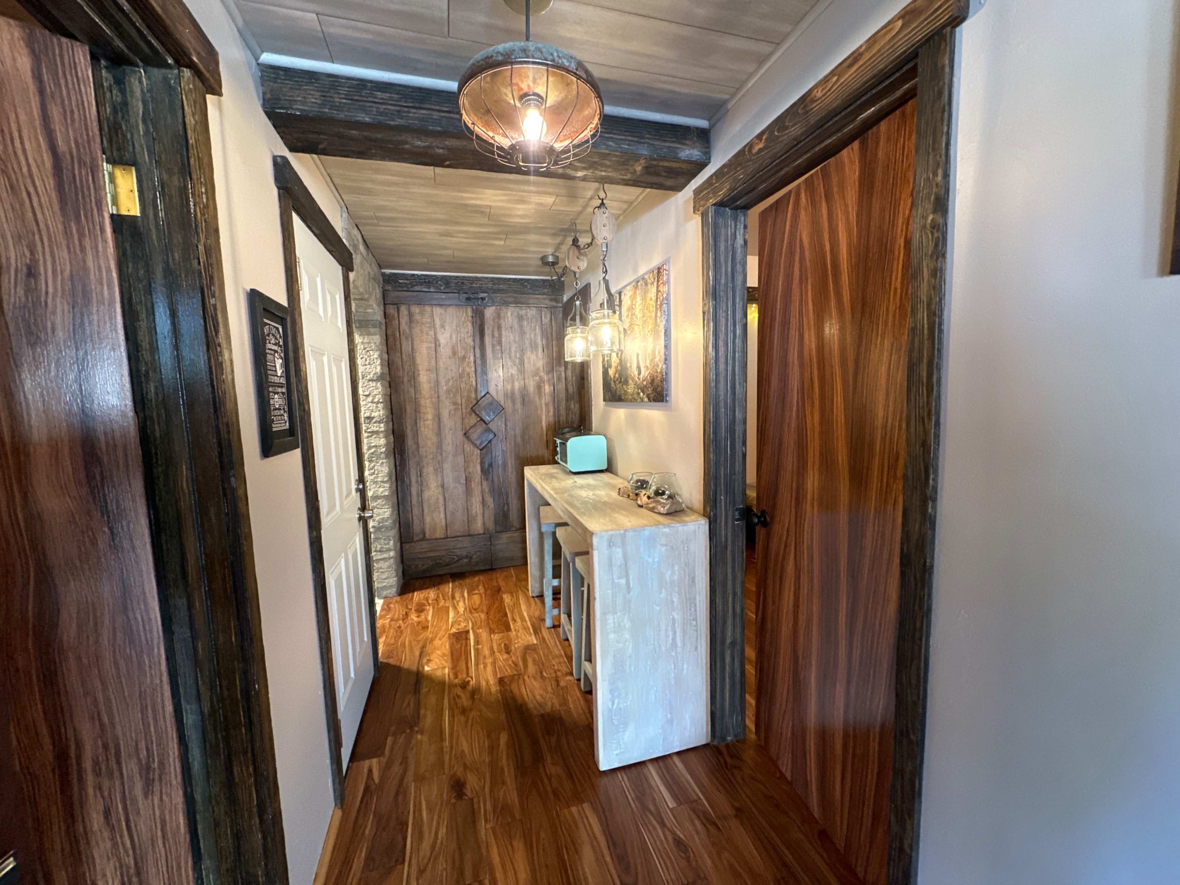 A hallway features wooden flooring, a console table under a light fixture, and doors leading to other rooms.