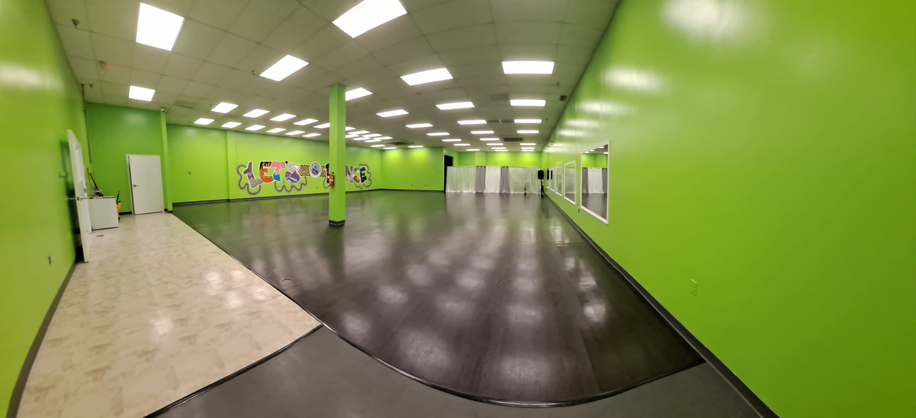 A spacious dance studio with vibrant green walls and a dark wooden floor.