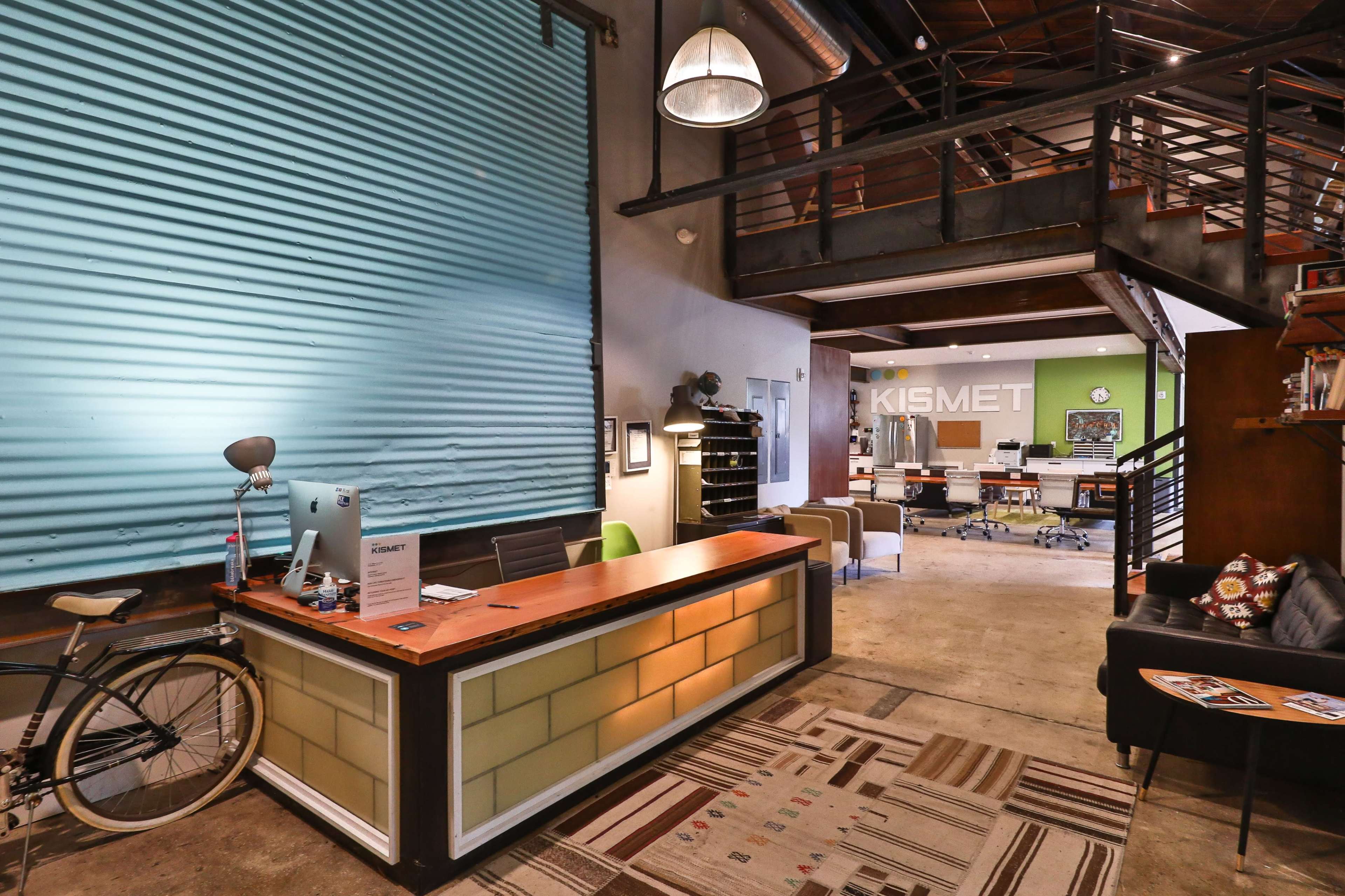 A modern office reception area featuring a wooden desk, a bicycle, and a spacious open workspace in the background.