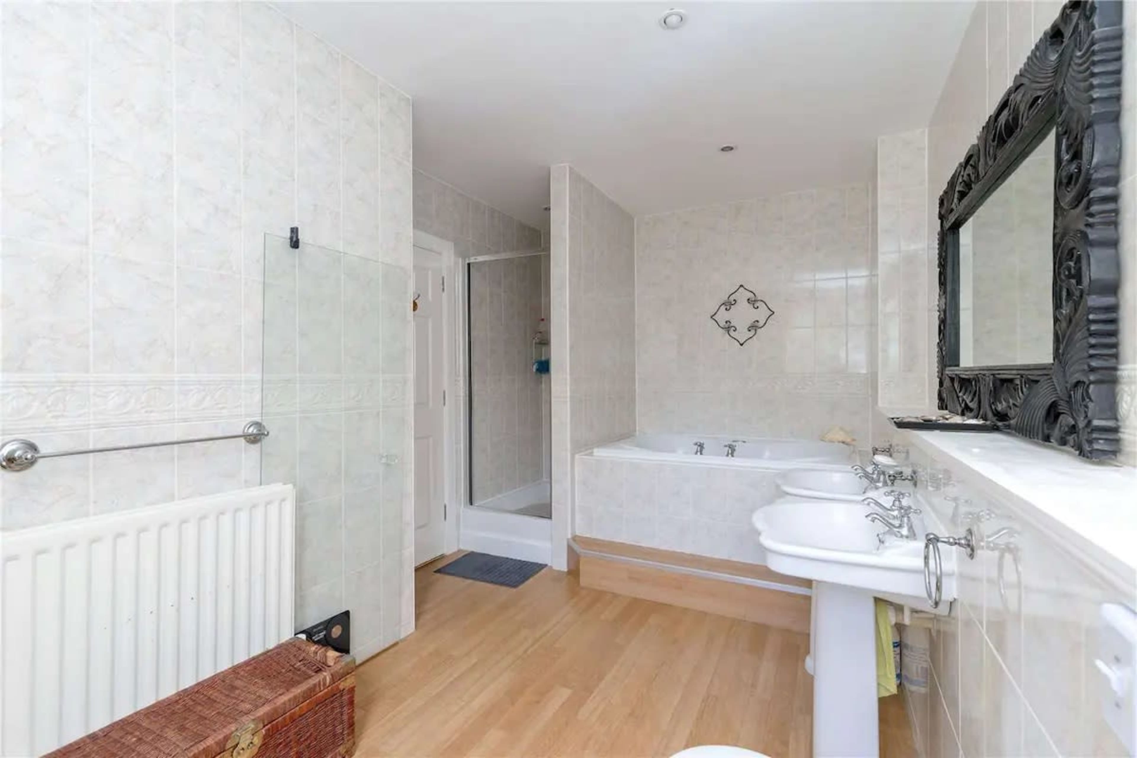A spacious bathroom featuring a bathtub, a walk-in shower, dual washbasins, and light-colored tiled walls.