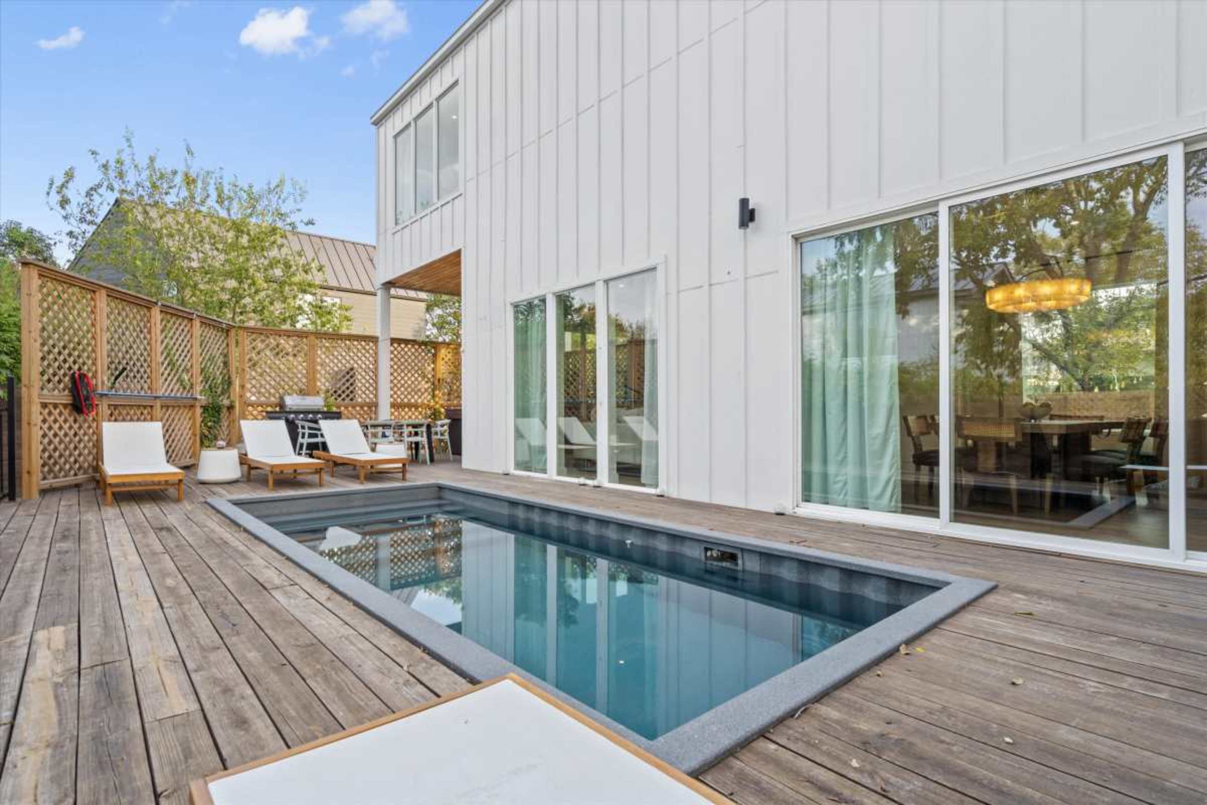 A modern home features a small pool surrounded by a wooden deck and lounge chairs.