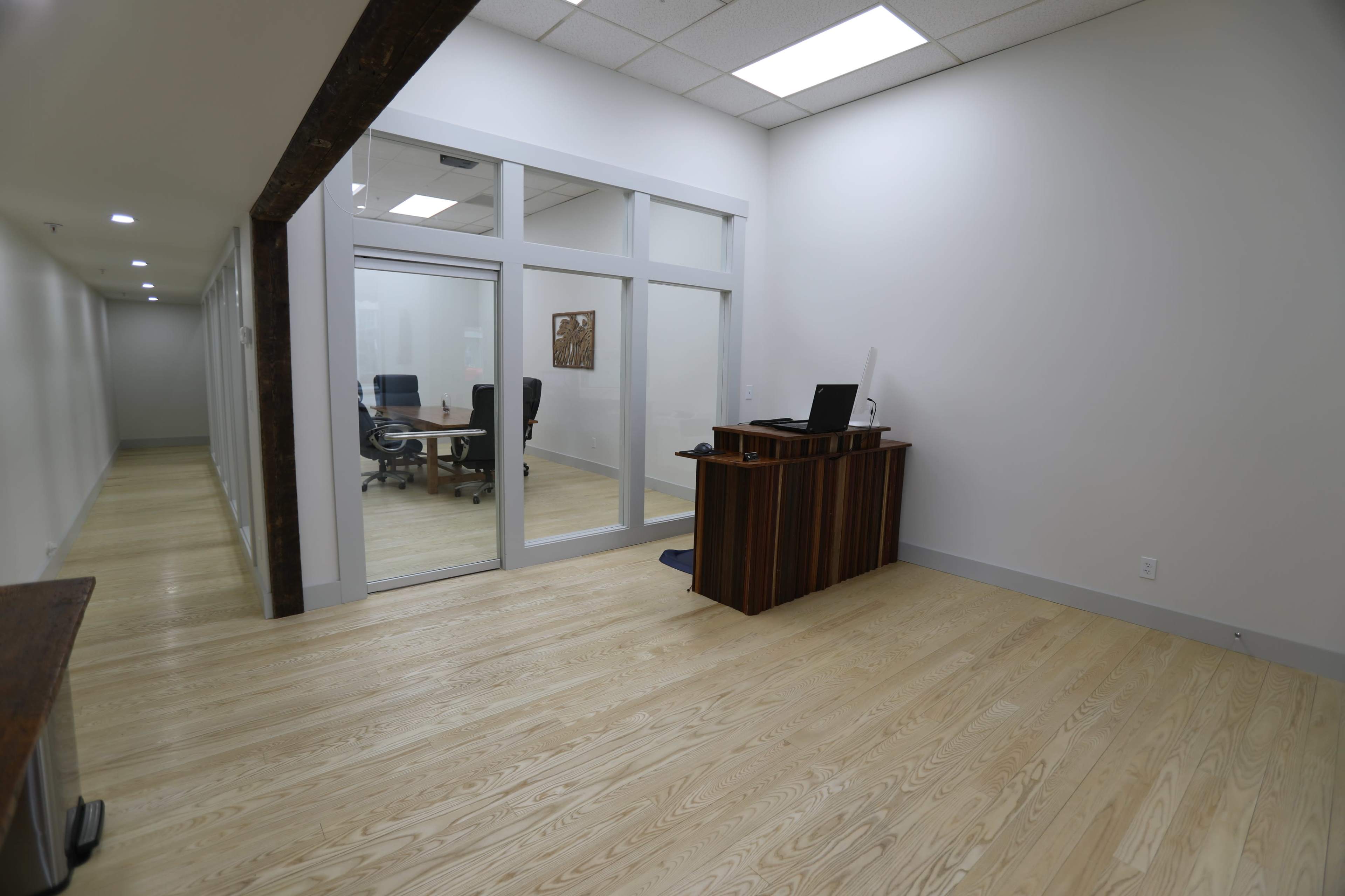 A bright office space with a wooden reception desk and a conference room visible through glass walls.