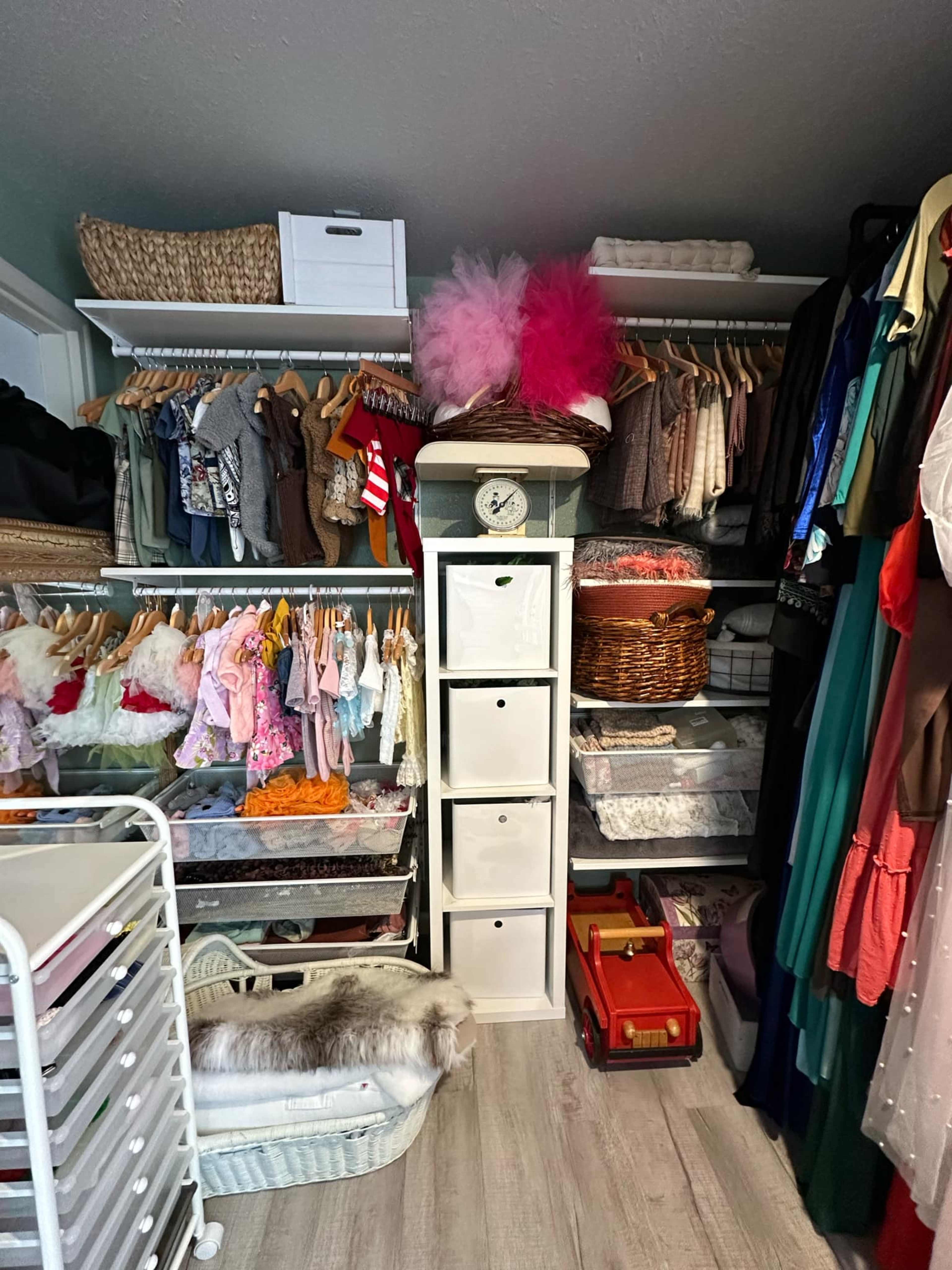 The image shows a neatly organized closet with various clothing items on hangers and shelves, along with storage bins and a toy truck.