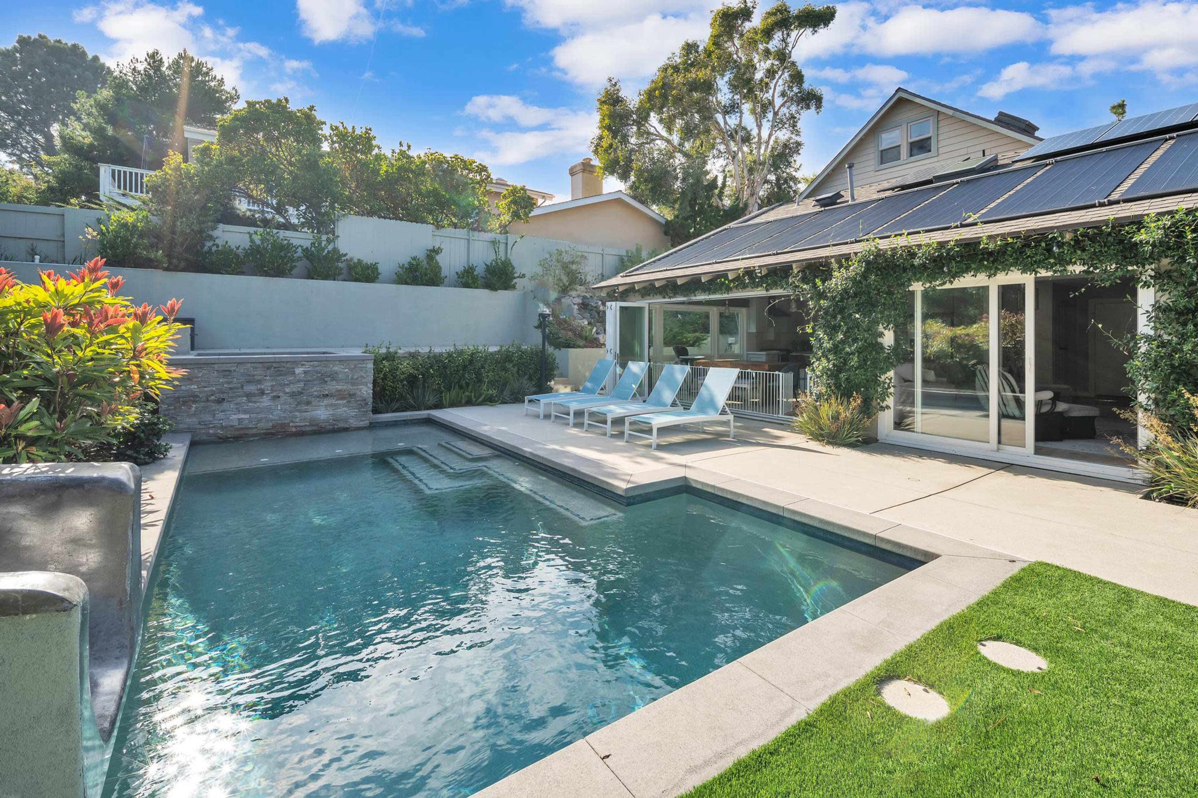 A modern home features a swimming pool surrounded by lounge chairs and landscaped greenery.
