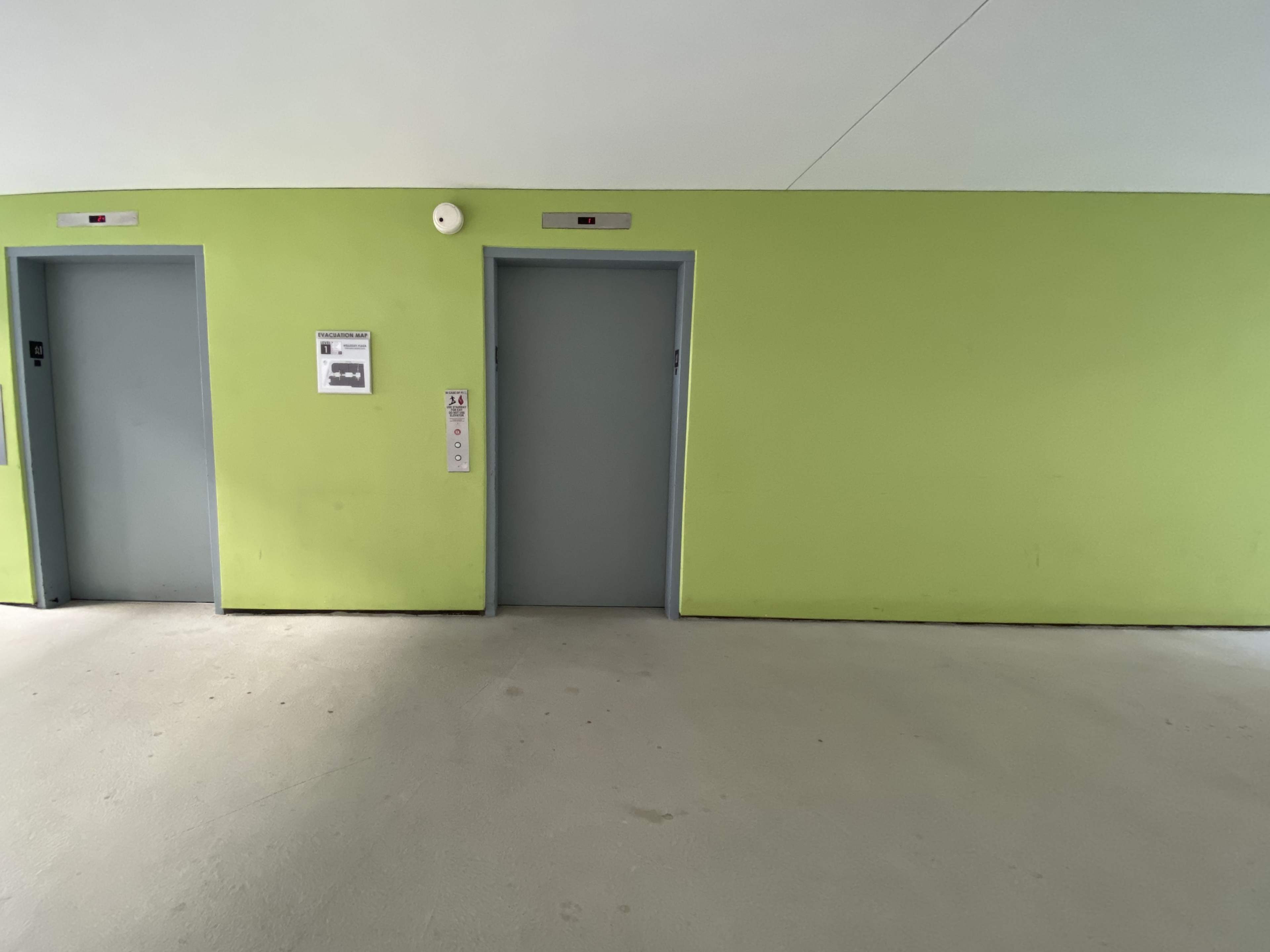 The image shows two gray elevator doors and a single door on a green wall in an interior hallway.