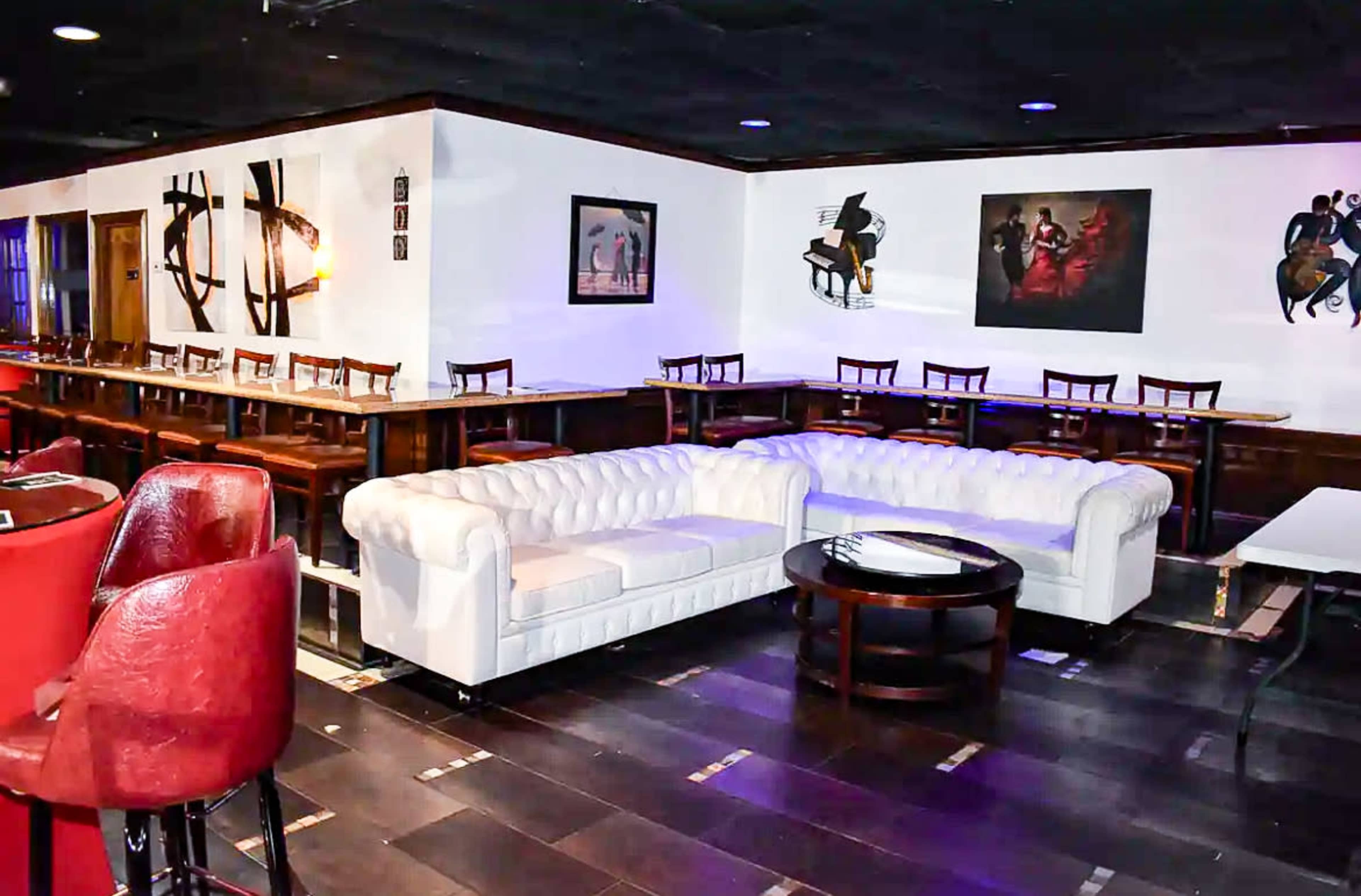 A spacious lounge features a white tufted sofa, a round table, and bar-style seating along the walls.