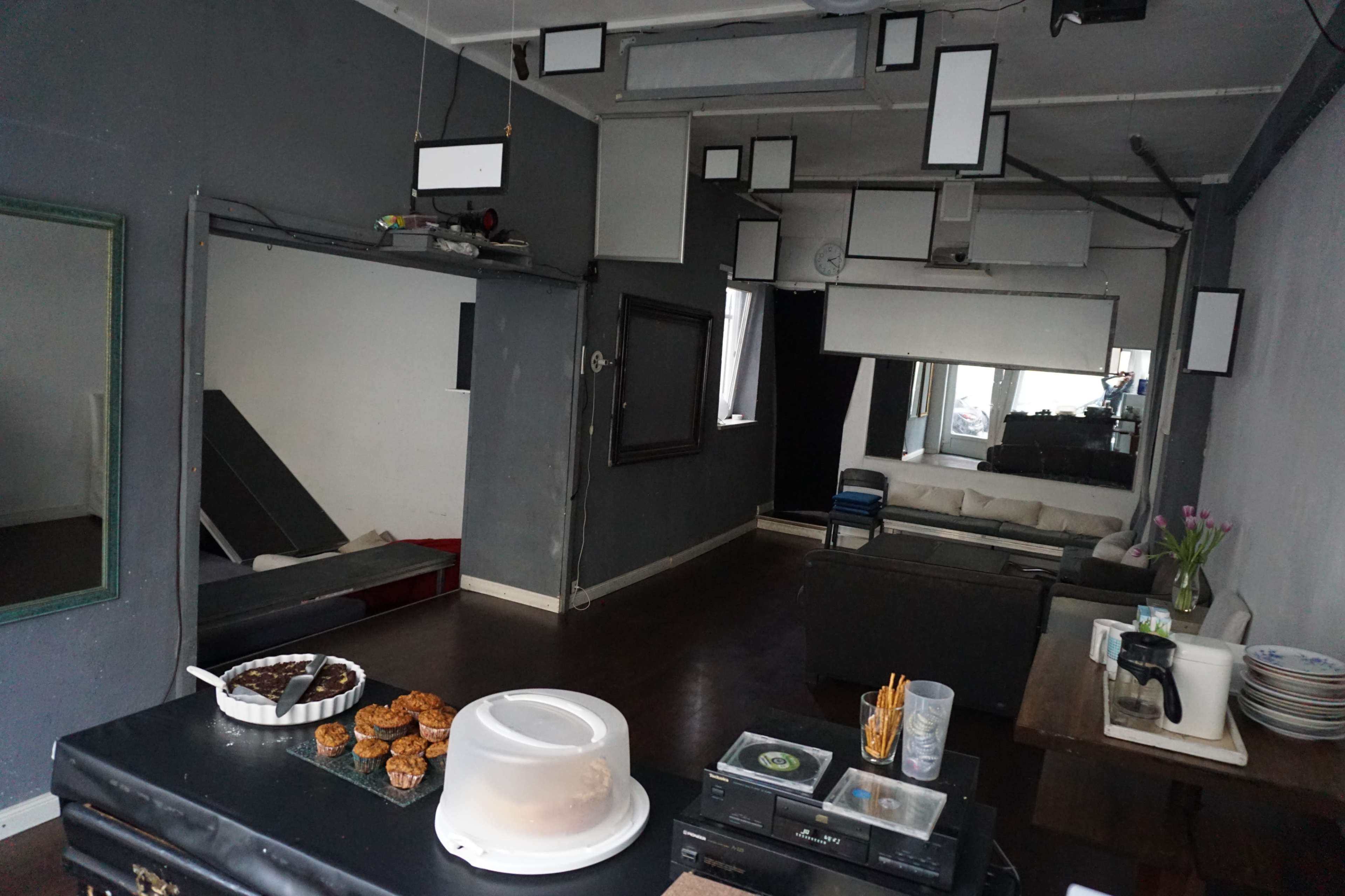 A spacious, gray-walled room with a couch, mirrors, and hanging light fixtures, featuring a table with baked goods in the foreground.