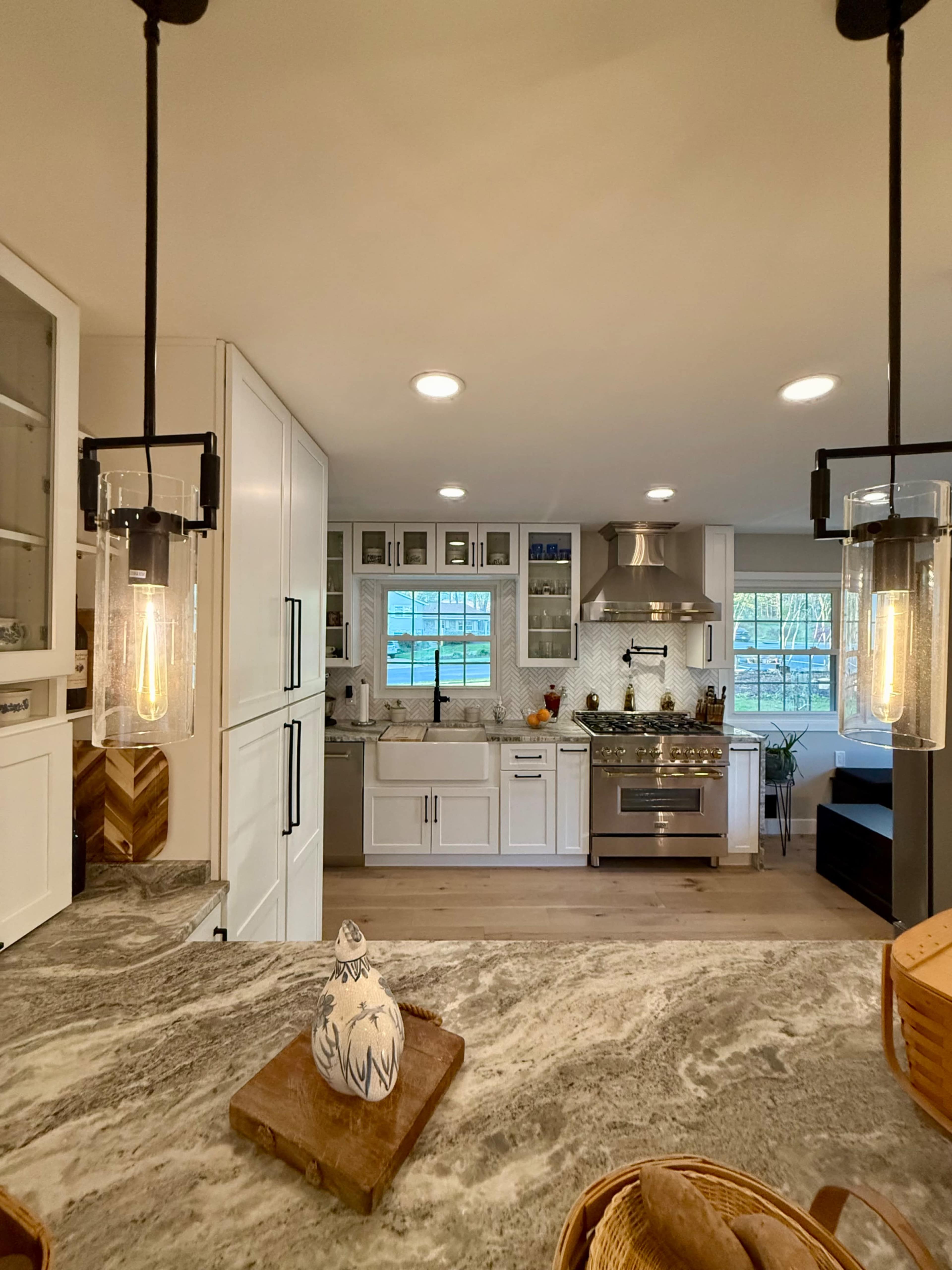 The image shows a modern kitchen with a marble countertop, pendant lighting, and stainless steel appliances.