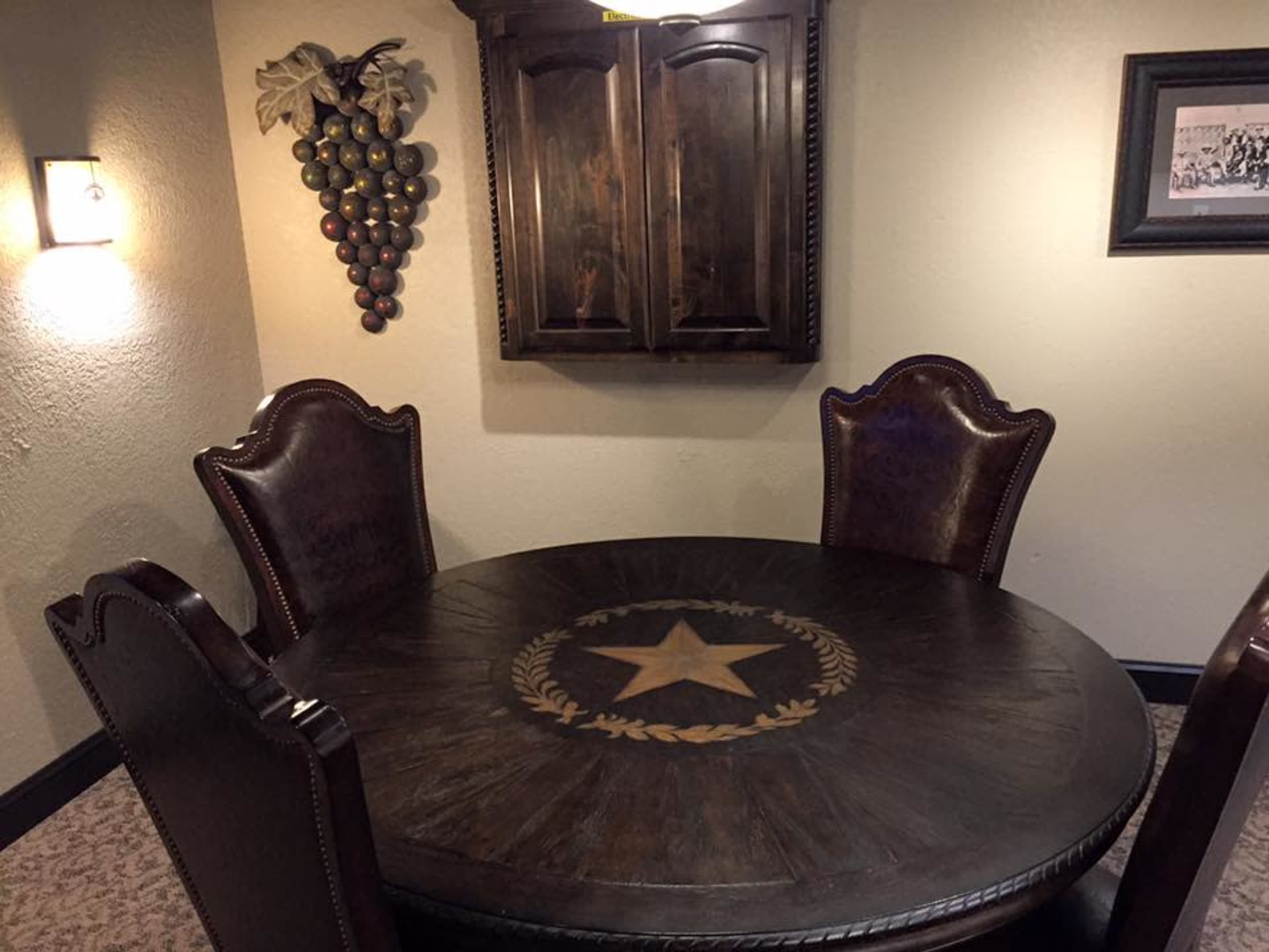 A round wooden dining table with a star and laurel design is accompanied by four dark leather chairs in a cozy, softly lit room.