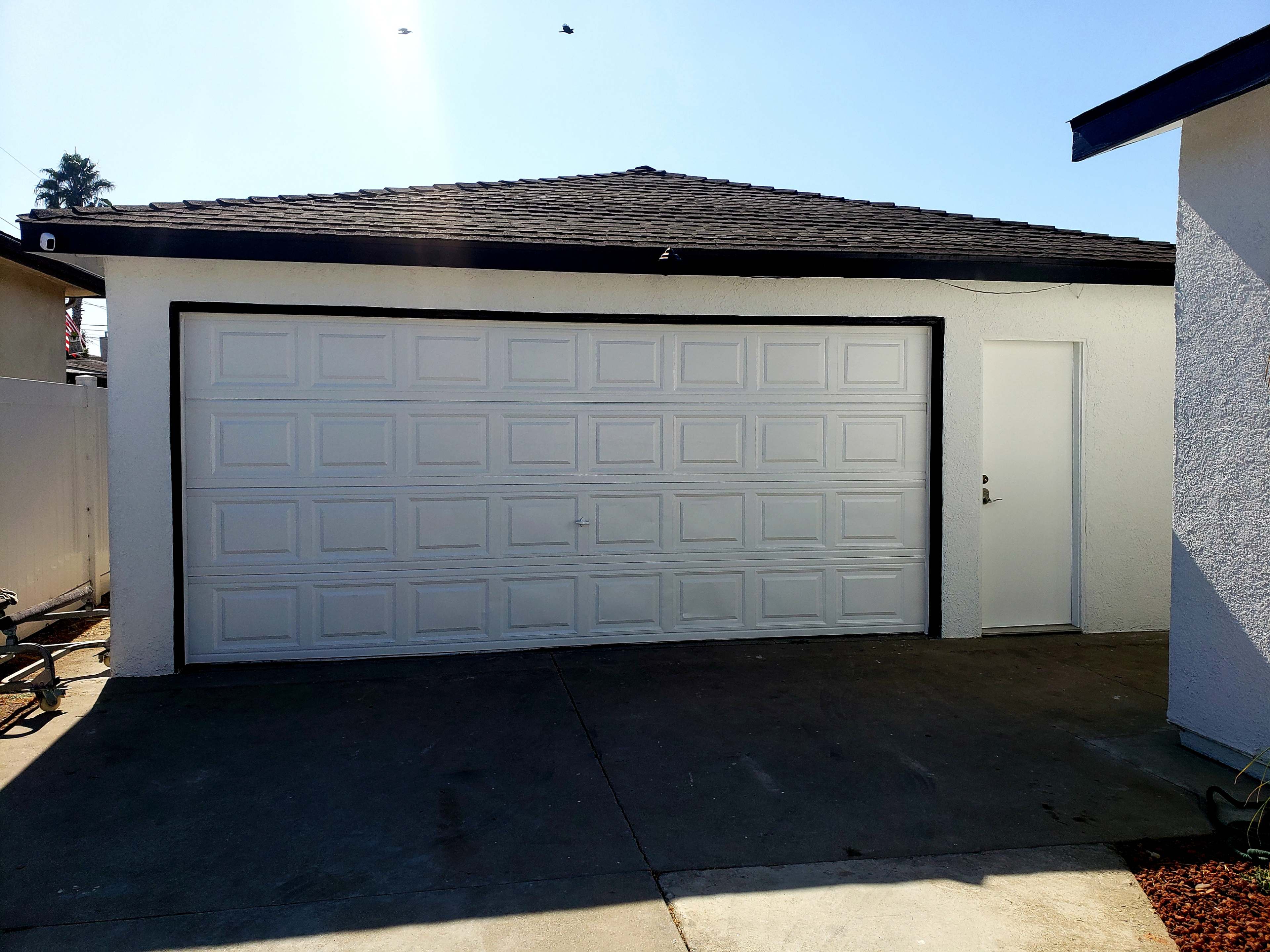 A white garage with a large door and a side entrance is set against a clear blue sky.
