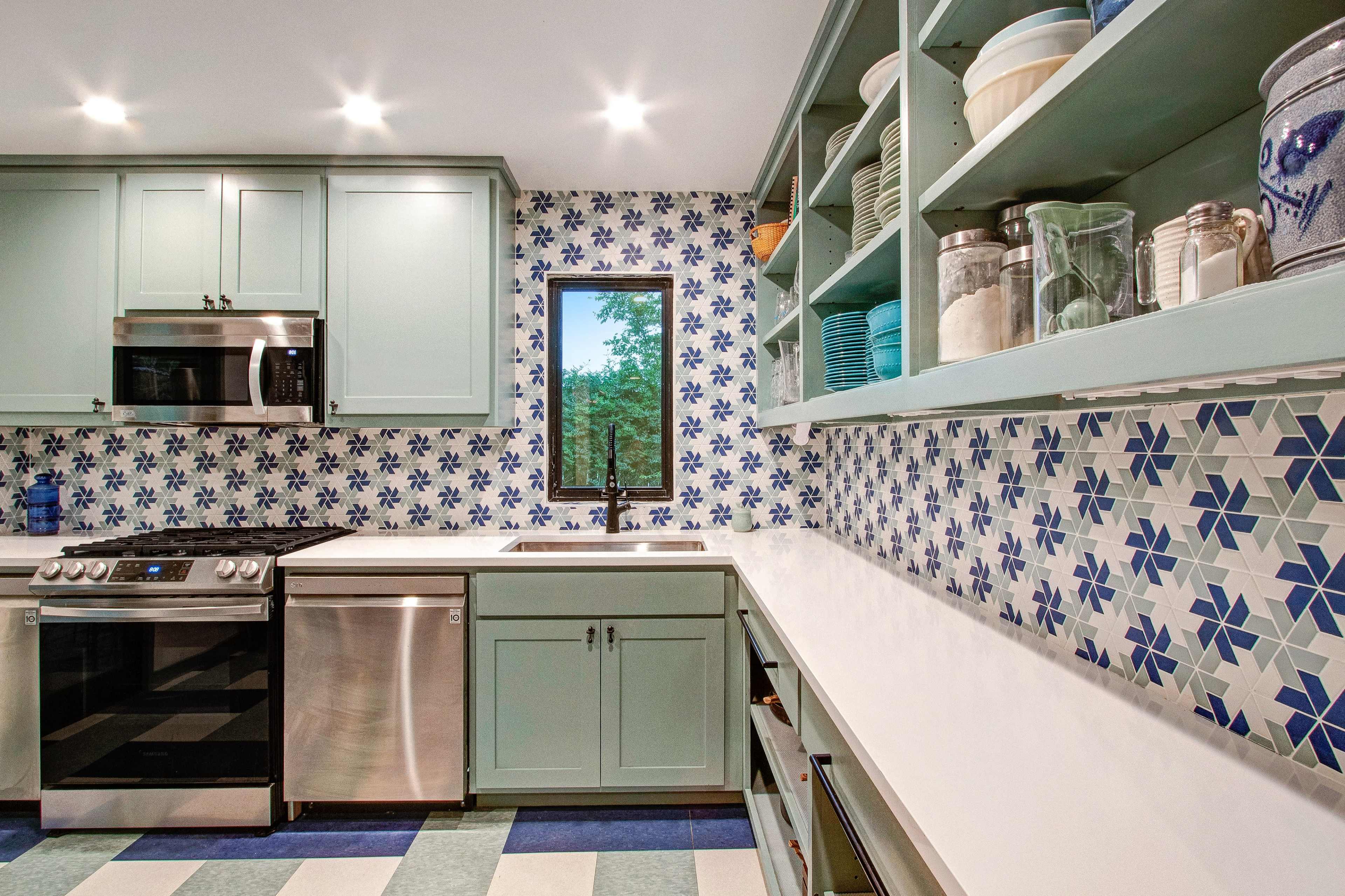 A modern kitchen features mint green cabinetry, a white countertop, and a patterned blue and white backsplash.