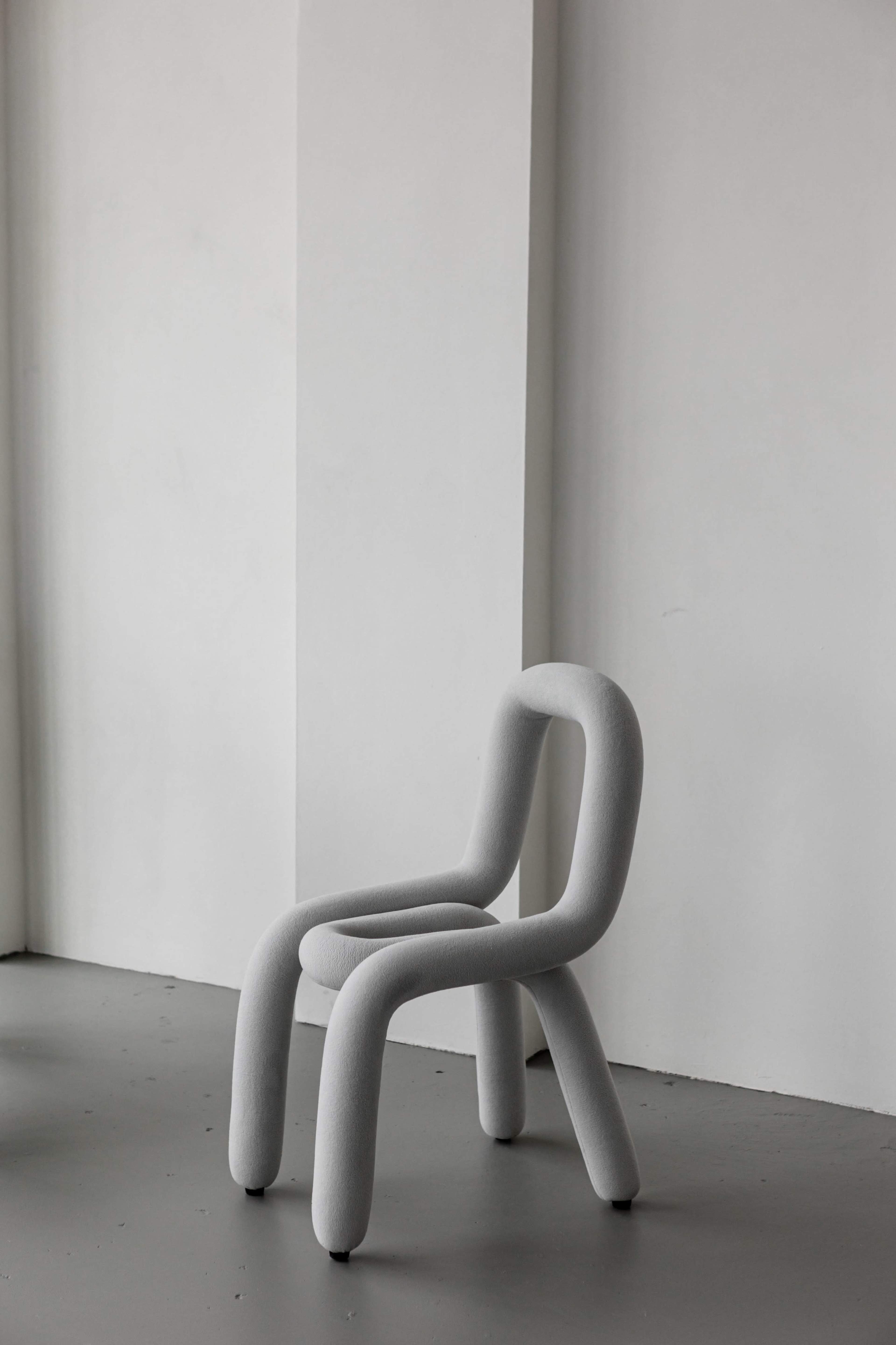A minimalist gray chair with curved legs and backrest placed against a plain wall.