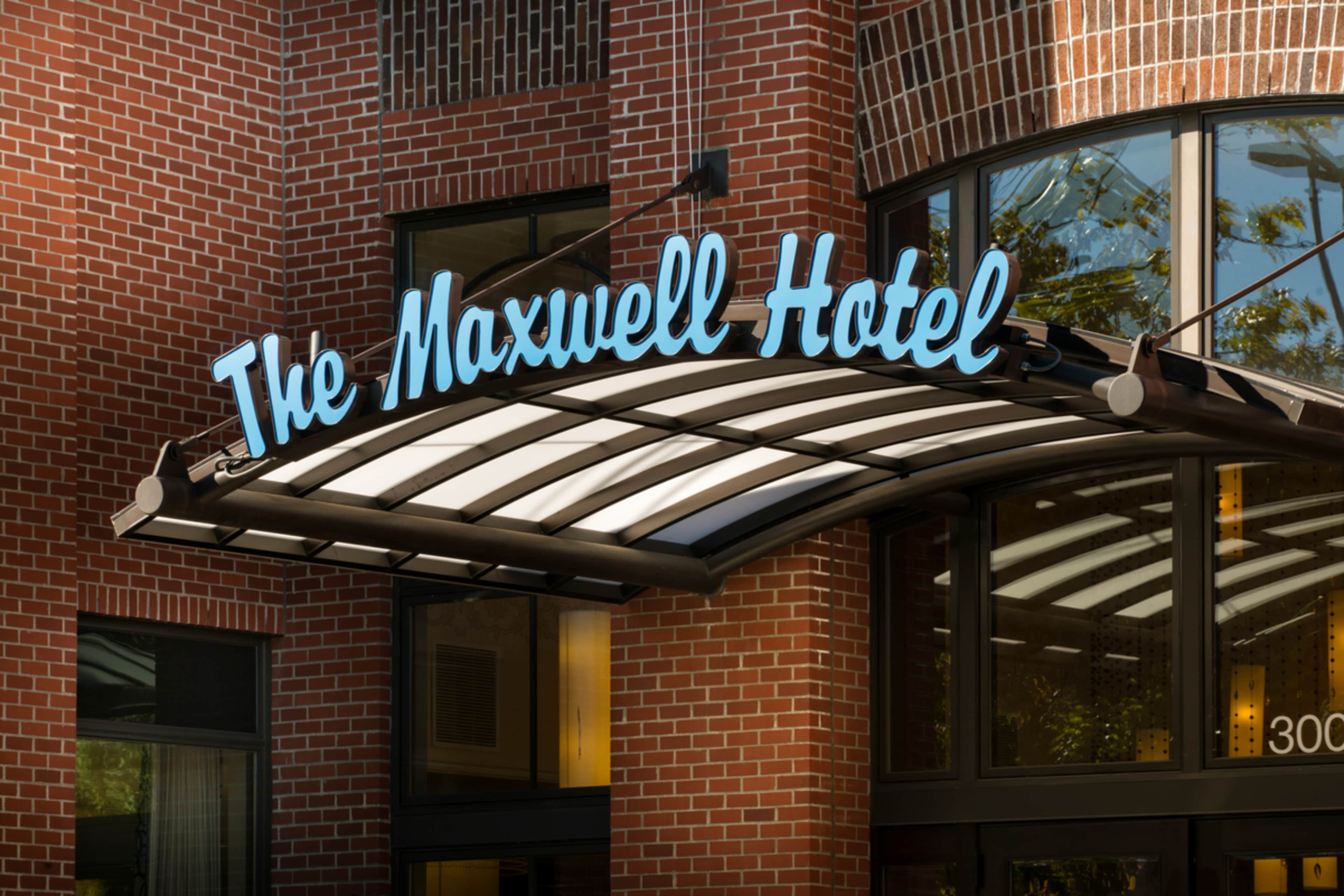 The exterior sign of The Maxwell Hotel, featuring a blue, illuminated name mounted above an entrance with a curved awning.