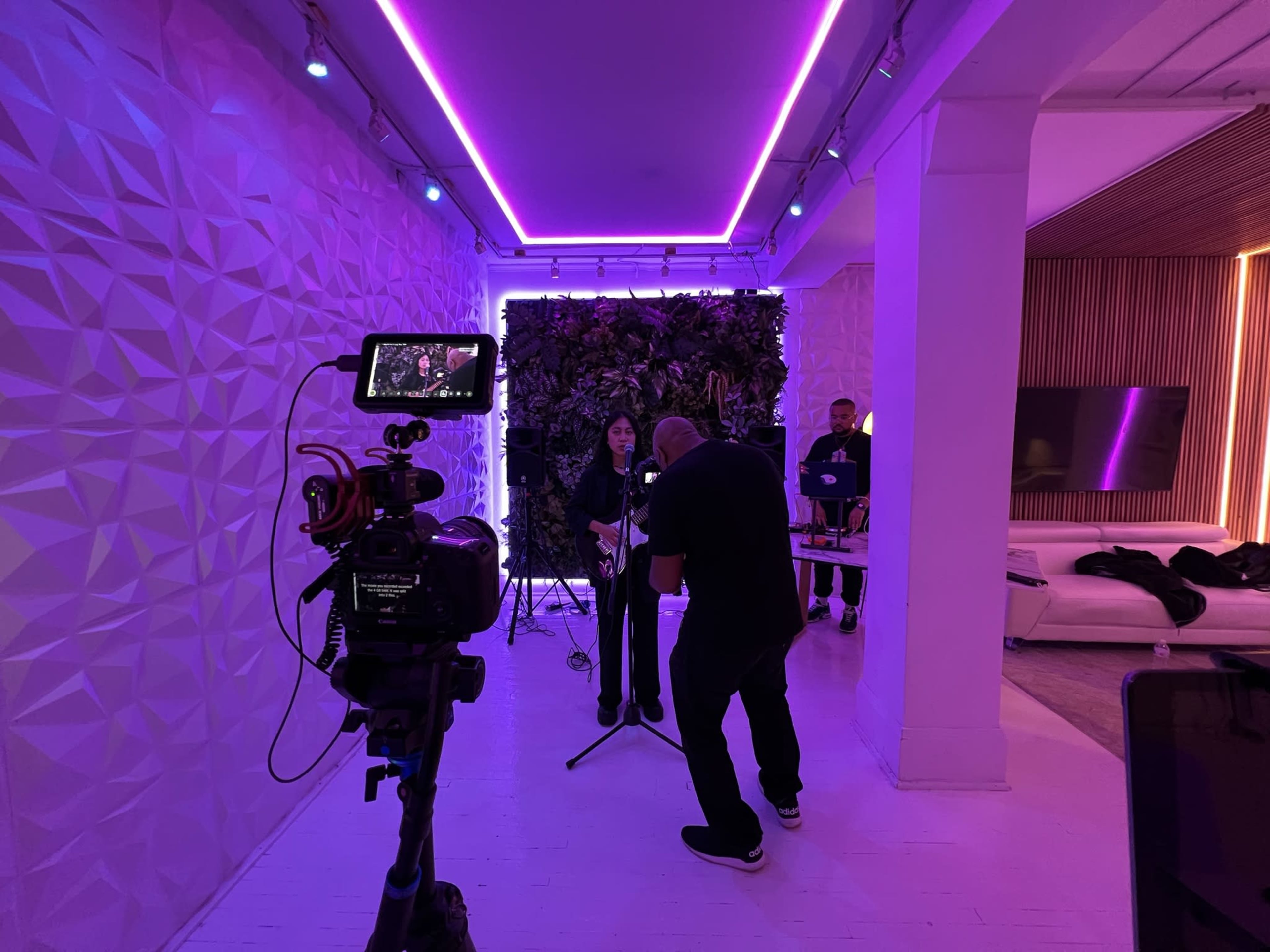 A singer performs in a modern studio with purple lighting while a videographer captures the scene.