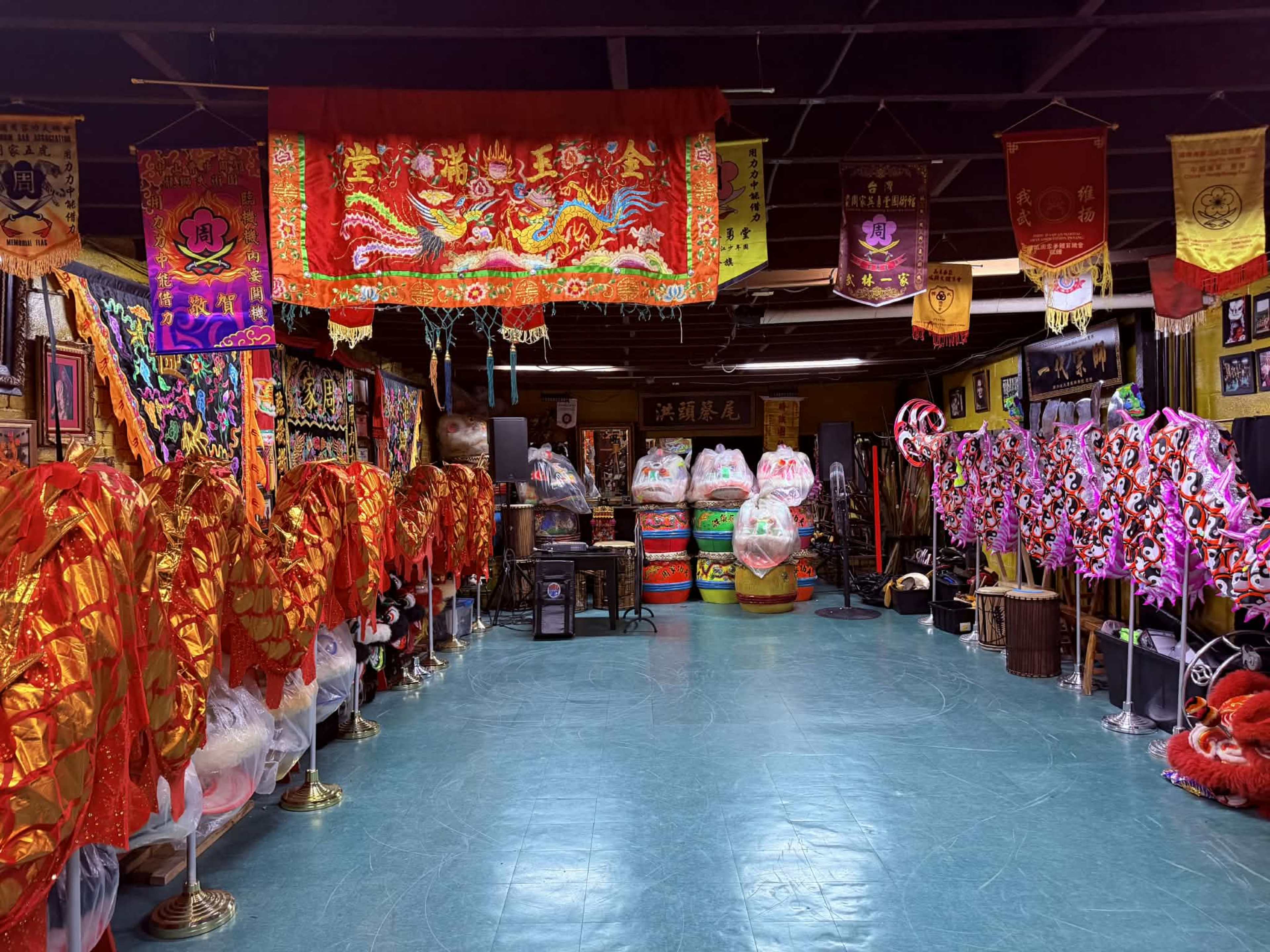 The image shows a vibrant indoor space filled with colorful decorations, including ornate lion dance costumes, banners, and various traditional items.