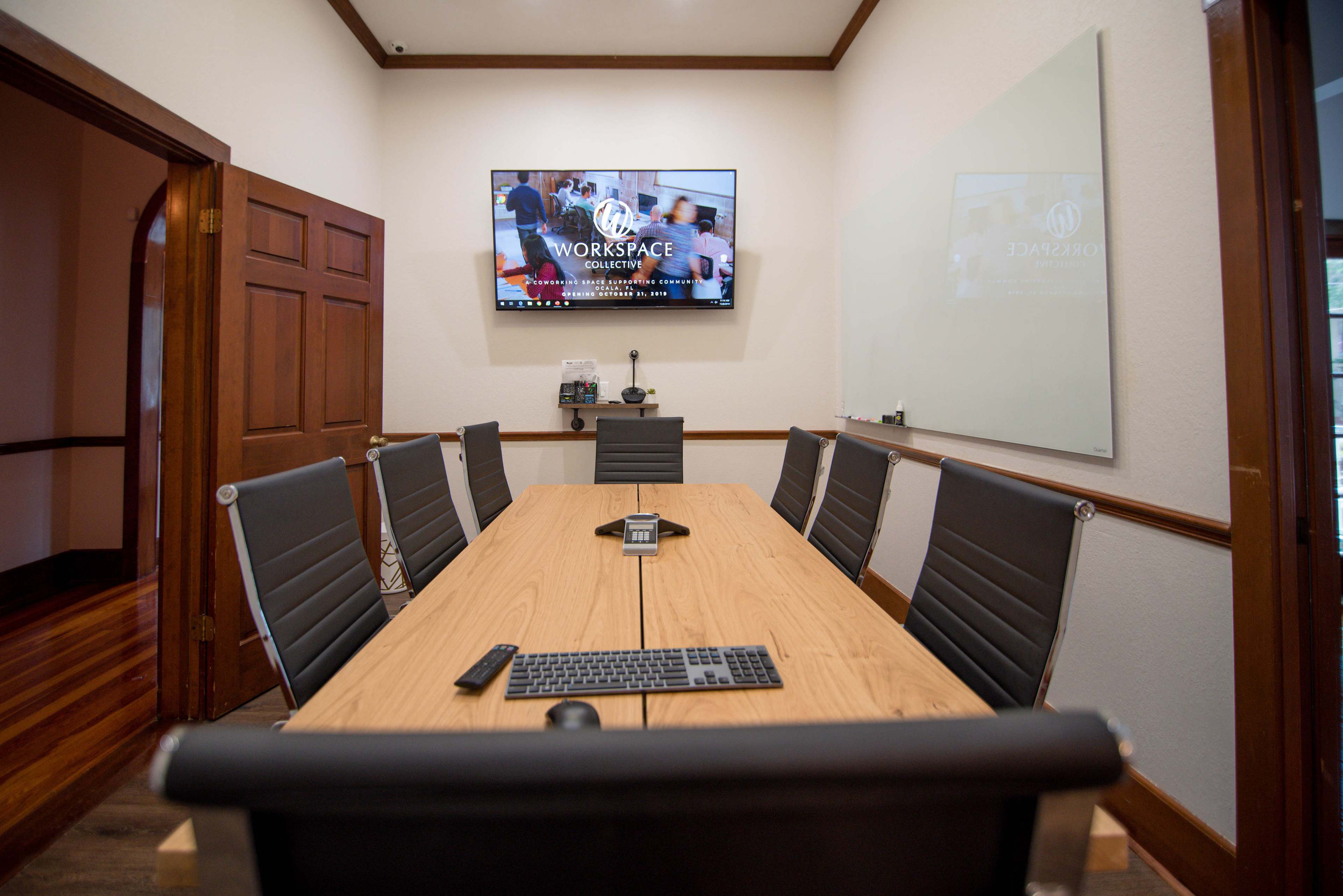 A modern conference room with a large wooden table, black chairs, and a wall-mounted screen displaying the word "WORKSPACE."