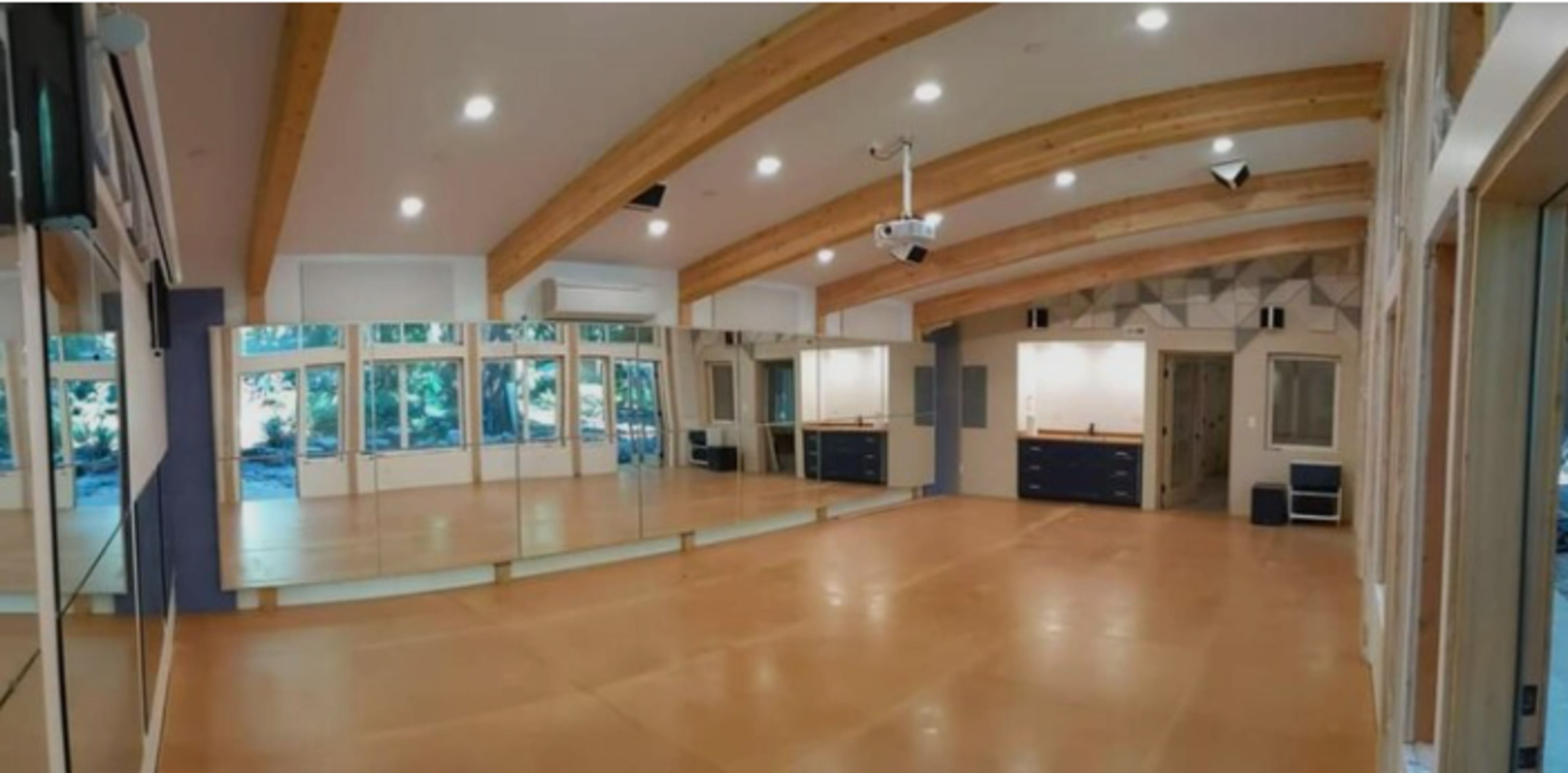 The image shows a spacious activity room with wooden beams, large windows, and a mirrored wall.