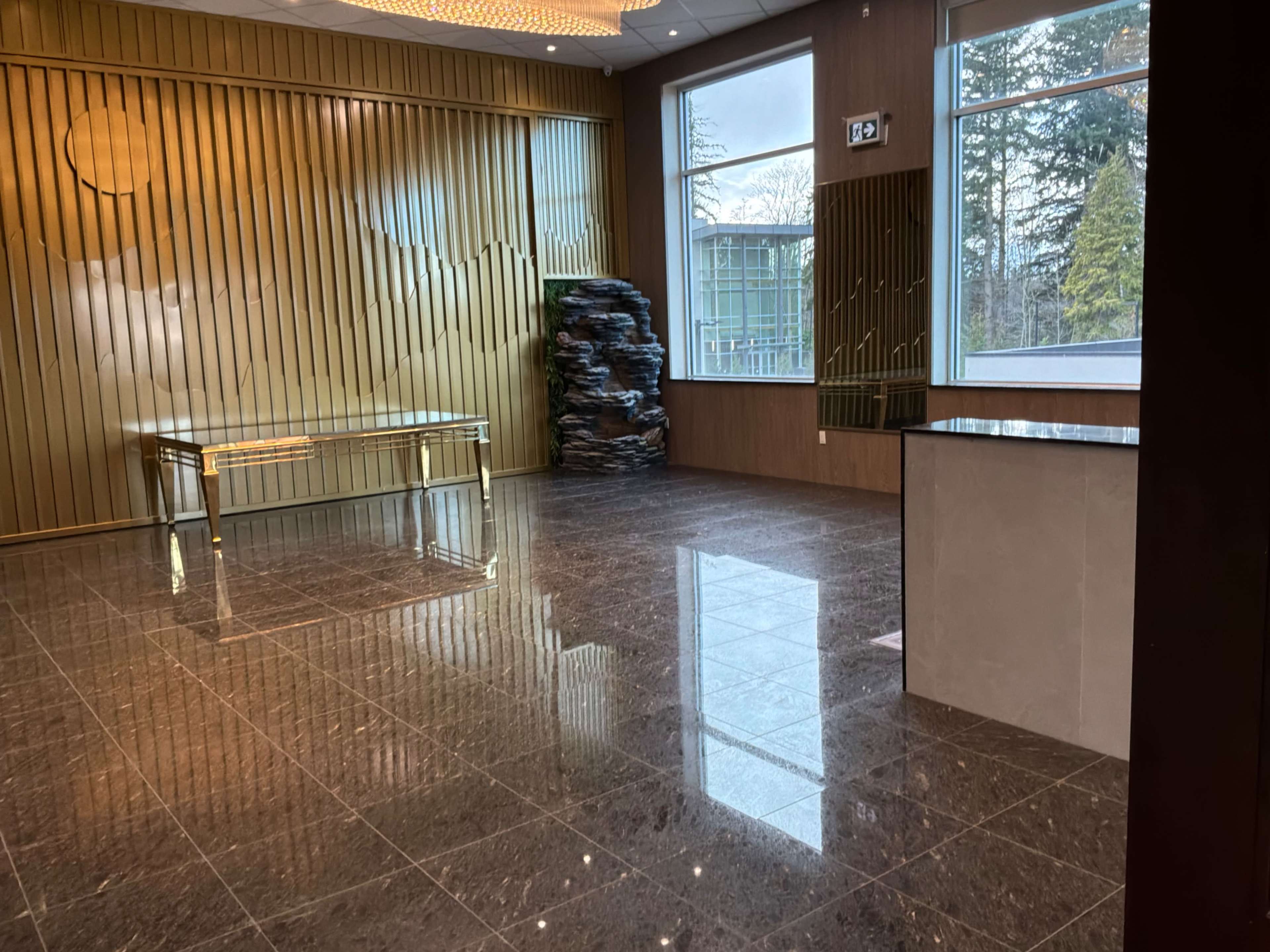 The image shows a modern interior space with a polished marble floor, a glass table, and a large window overlooking trees outside.