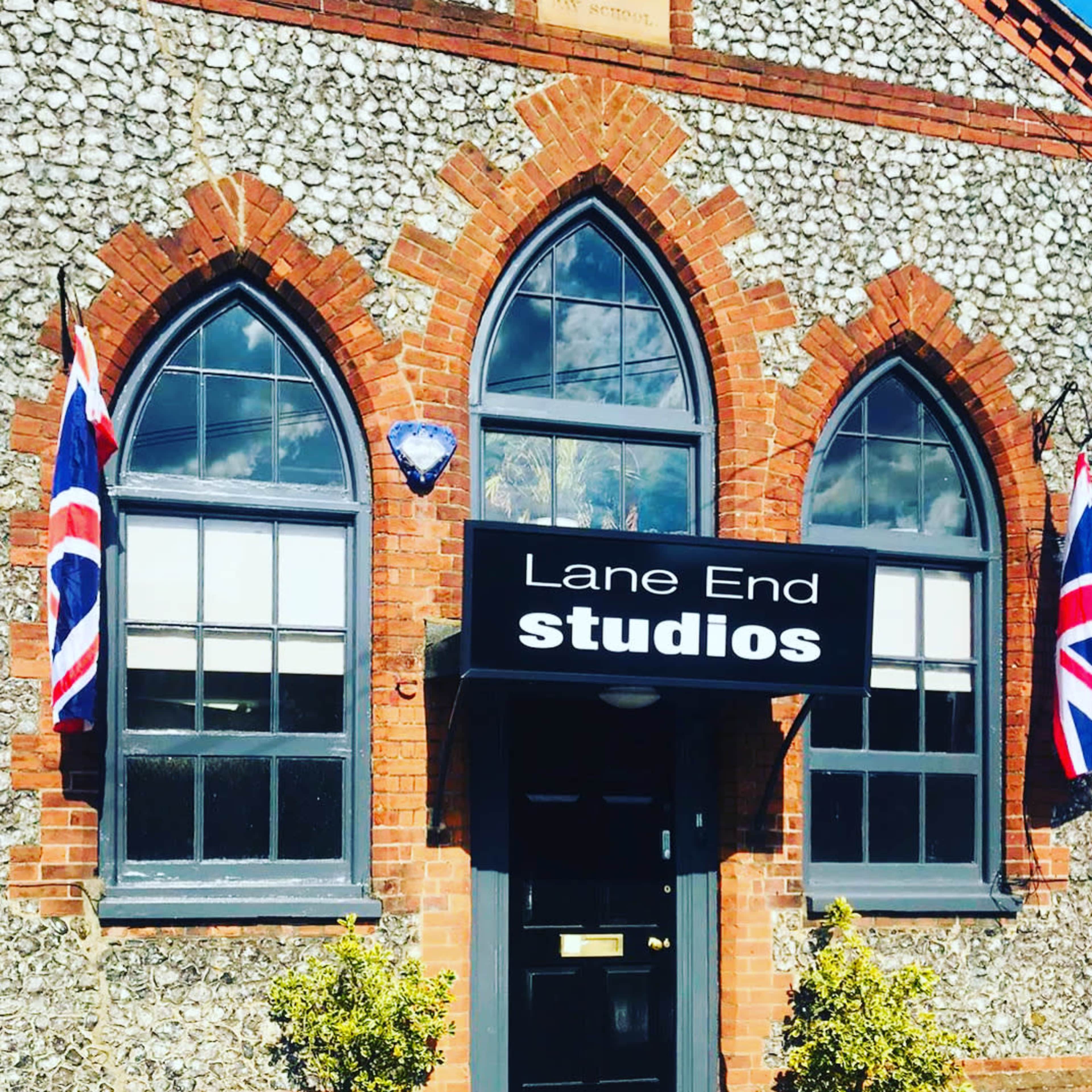 A brick building with arched windows, featuring a sign that reads "Lane End Studios" and adorned with Union Jack flags.