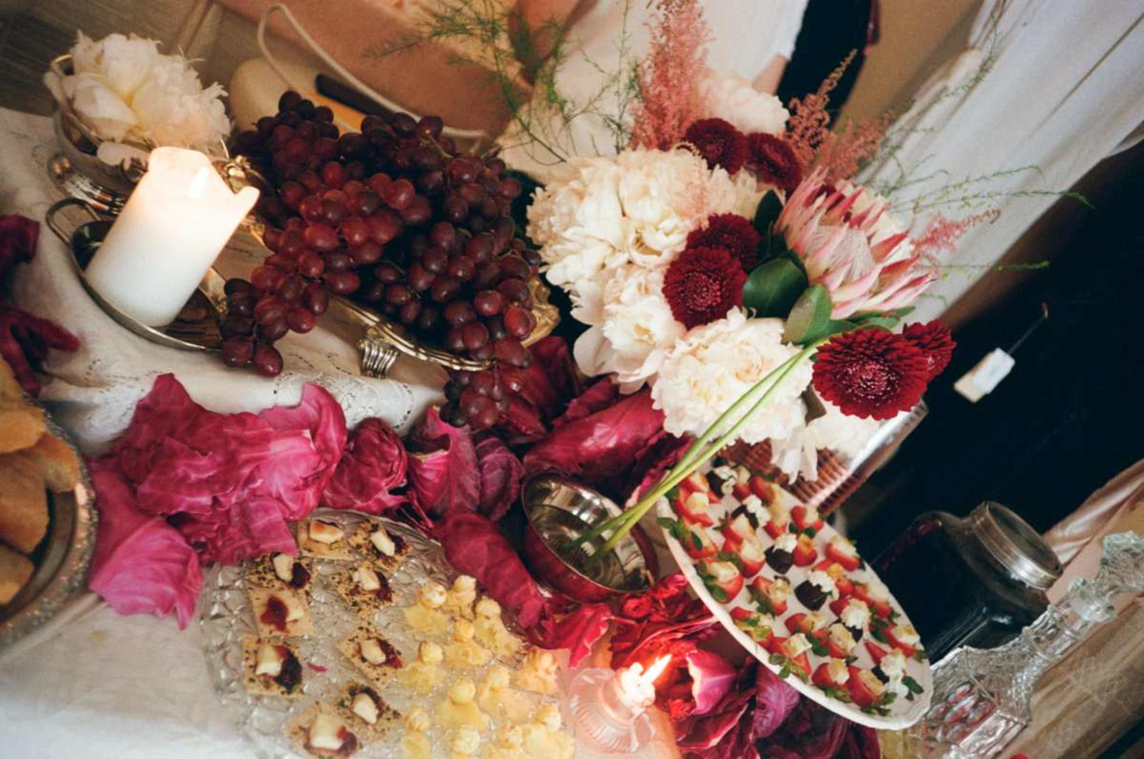 The image features a decorated table with an assortment of fruits, floral arrangements, and various desserts arranged elegantly.