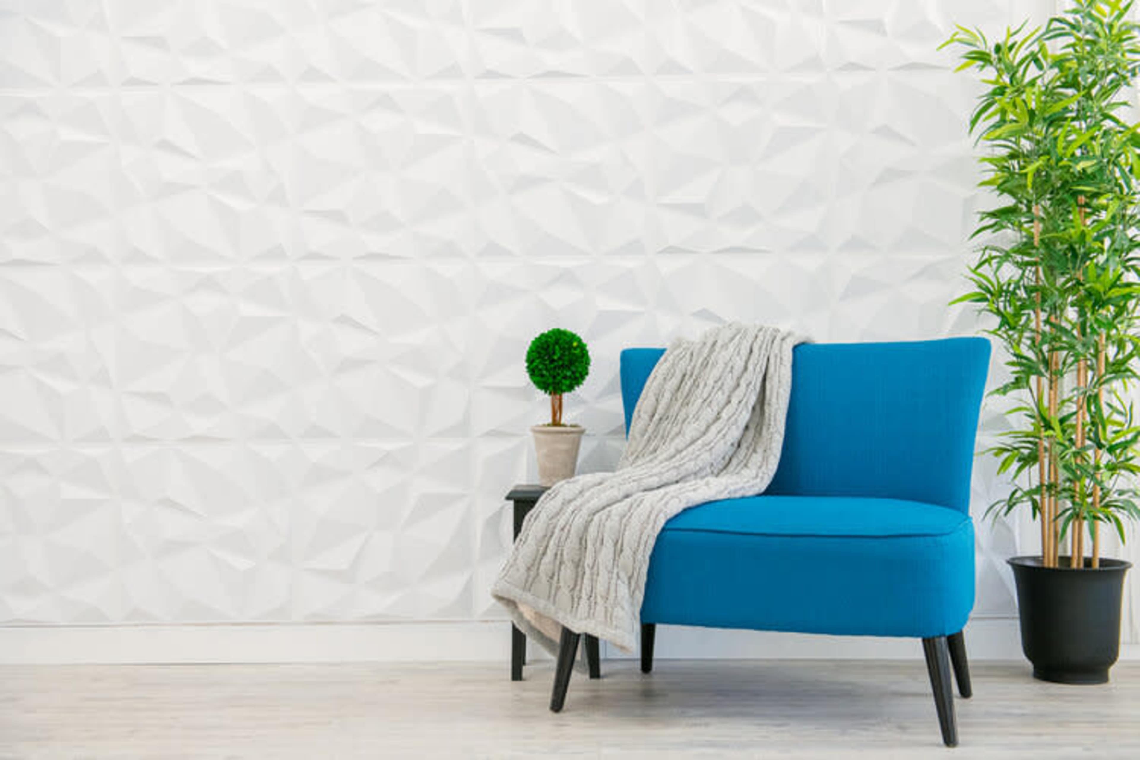 A blue sofa with a gray throw blanket sits next to a small table and a potted plant against a textured white wall.