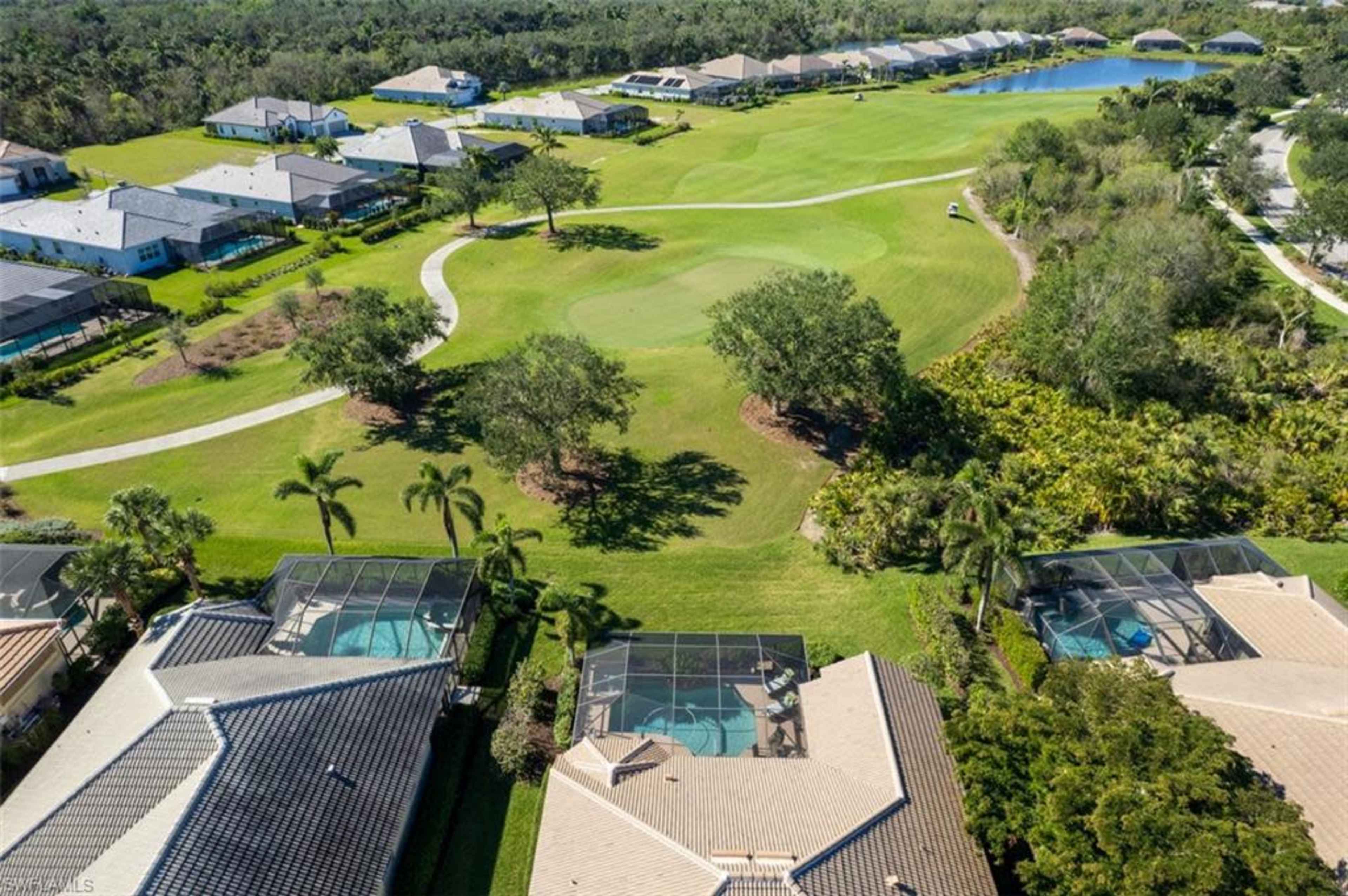 A bird's-eye view of residential homes with swimming pools, a golf course, and a winding pathway surrounded by greenery.