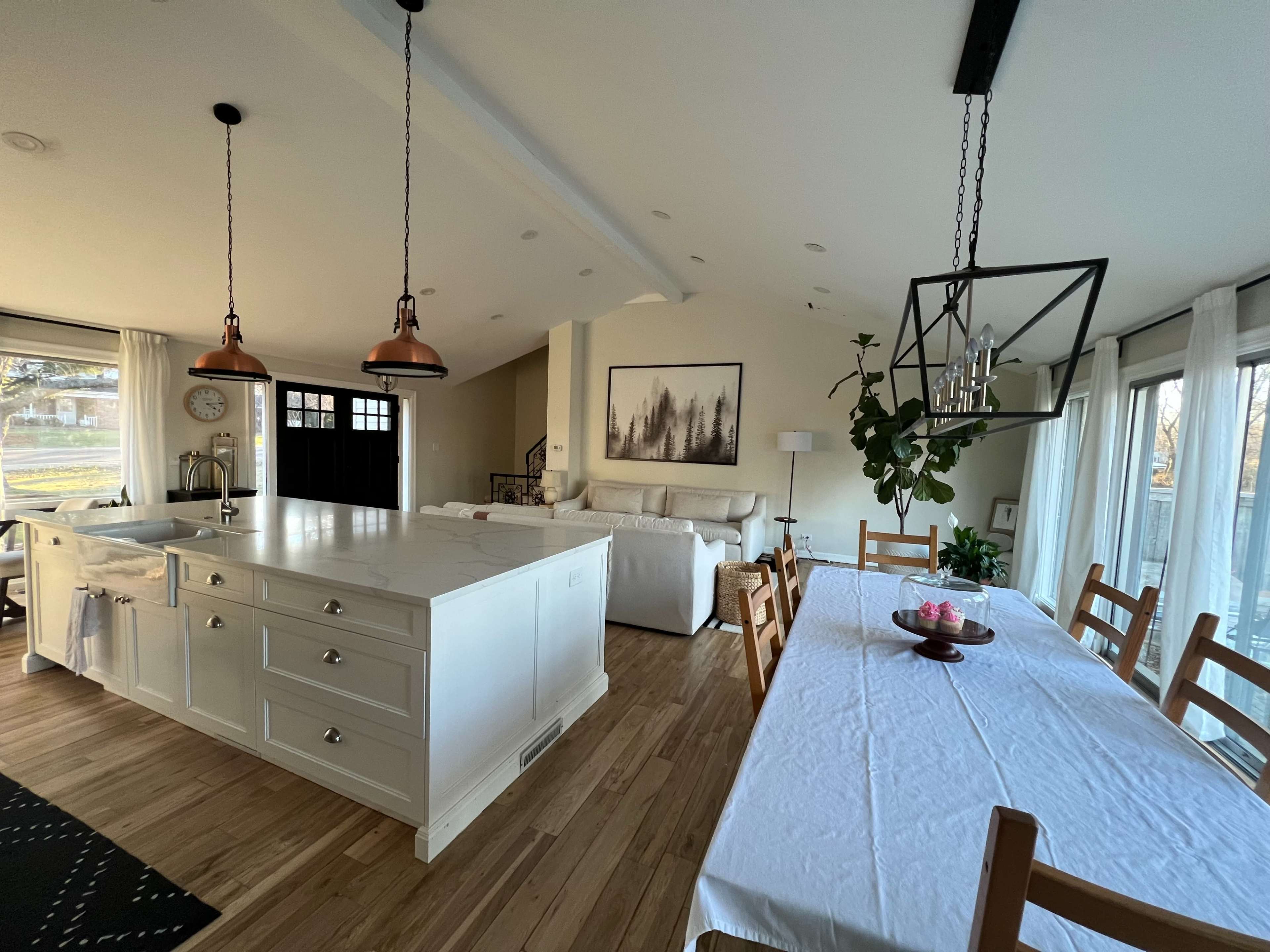 An open-concept kitchen and dining area featuring a large island with a white countertop, wooden dining table, and modern lighting fixtures.