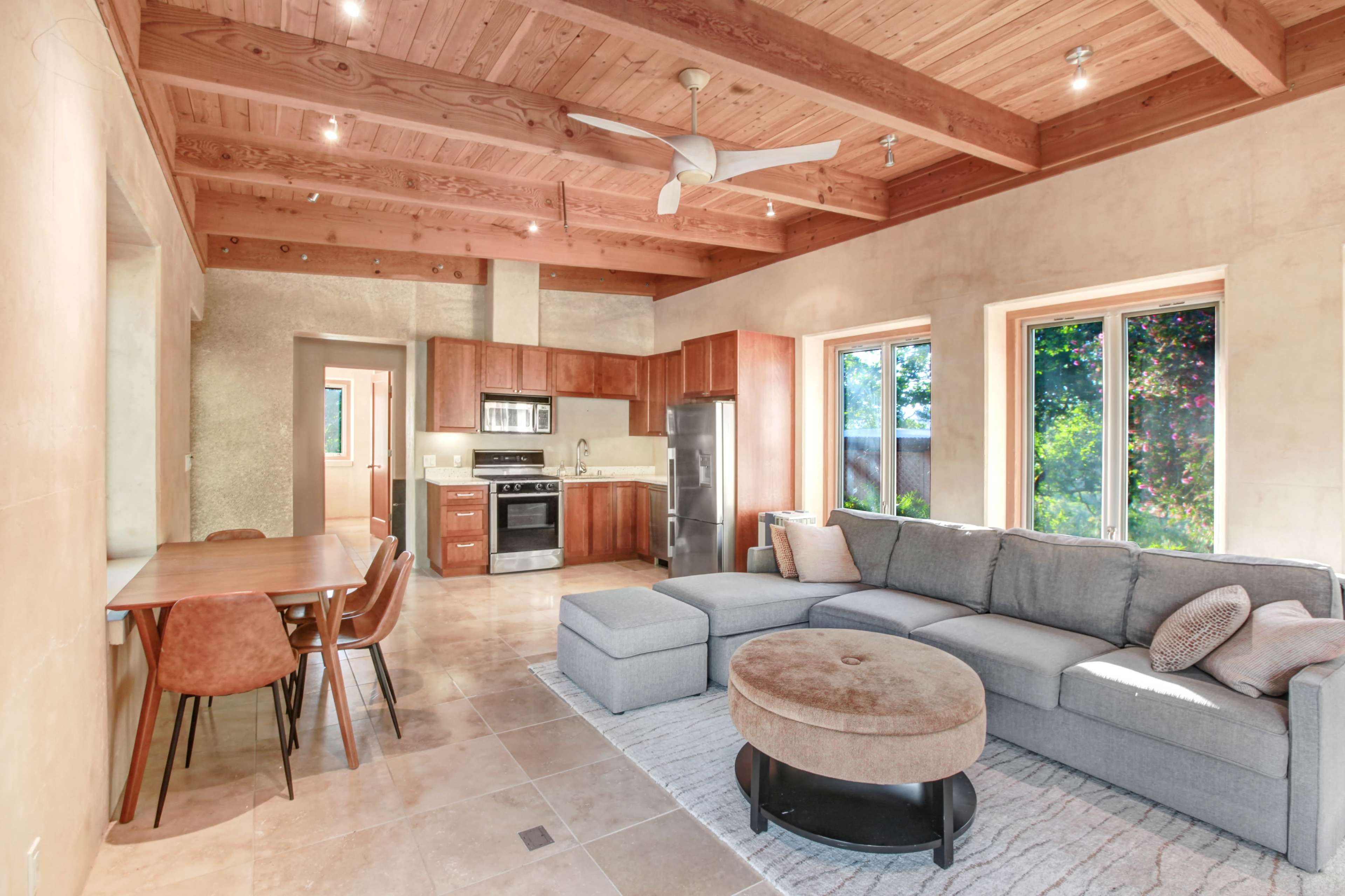 A modern living space with a sectional sofa, a round coffee table, a dining table with chairs, and a kitchen area visible in the background.