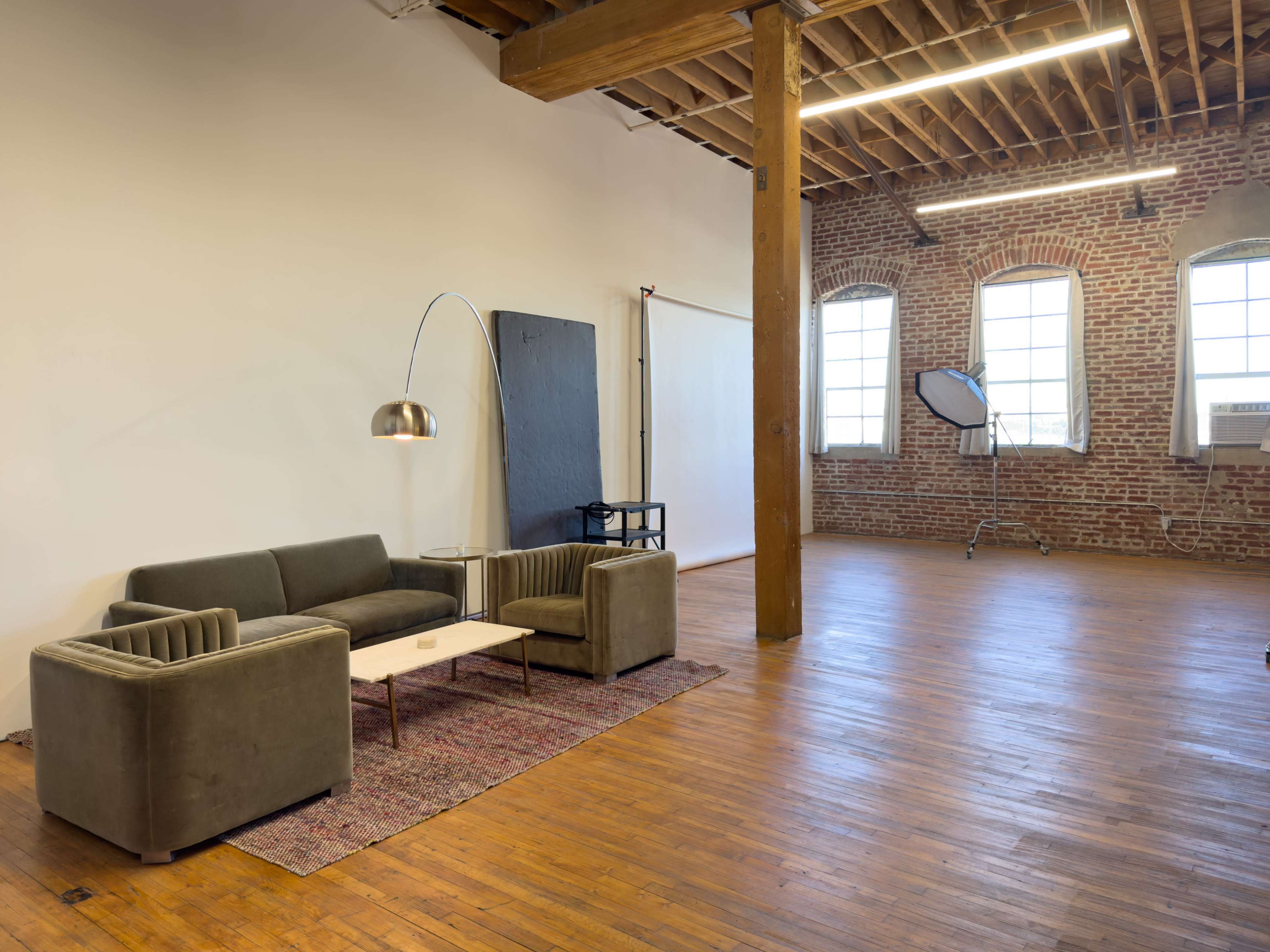 The image shows a spacious interior with exposed brick walls, wooden floors, and a modern sofa set in a well-lit room.