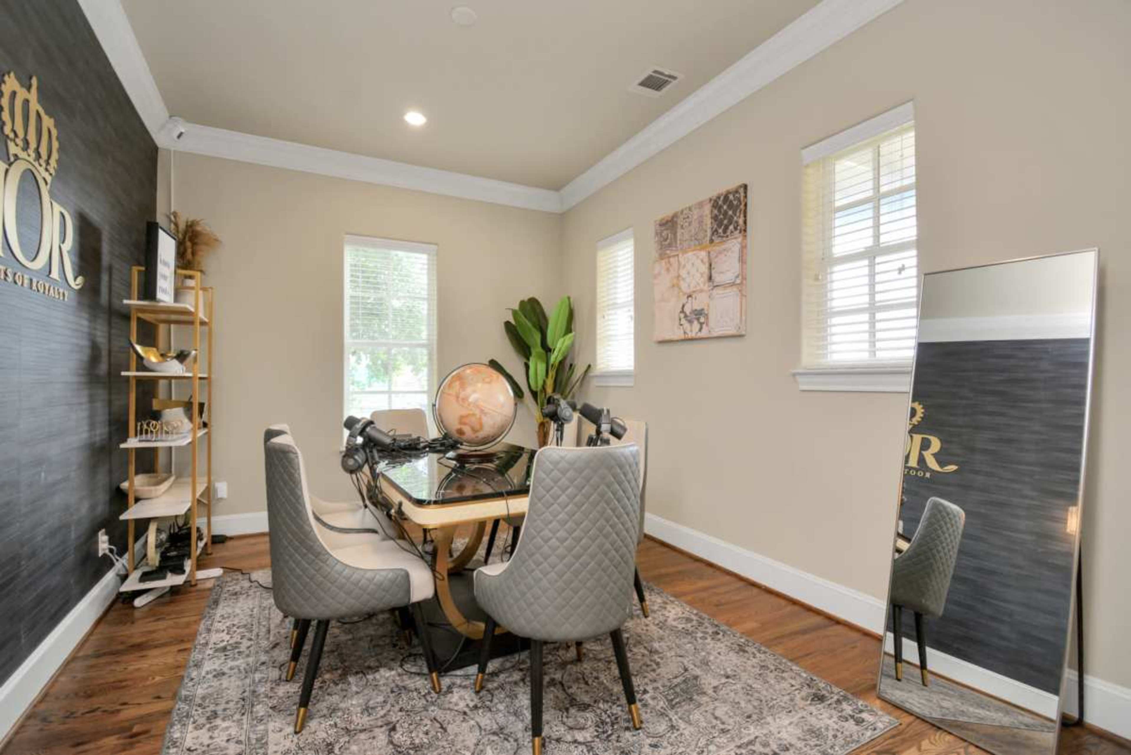 The image shows a modern office space featuring a glass-top dining table surrounded by six upholstered chairs, a large mirror, and decorative elements on the walls.