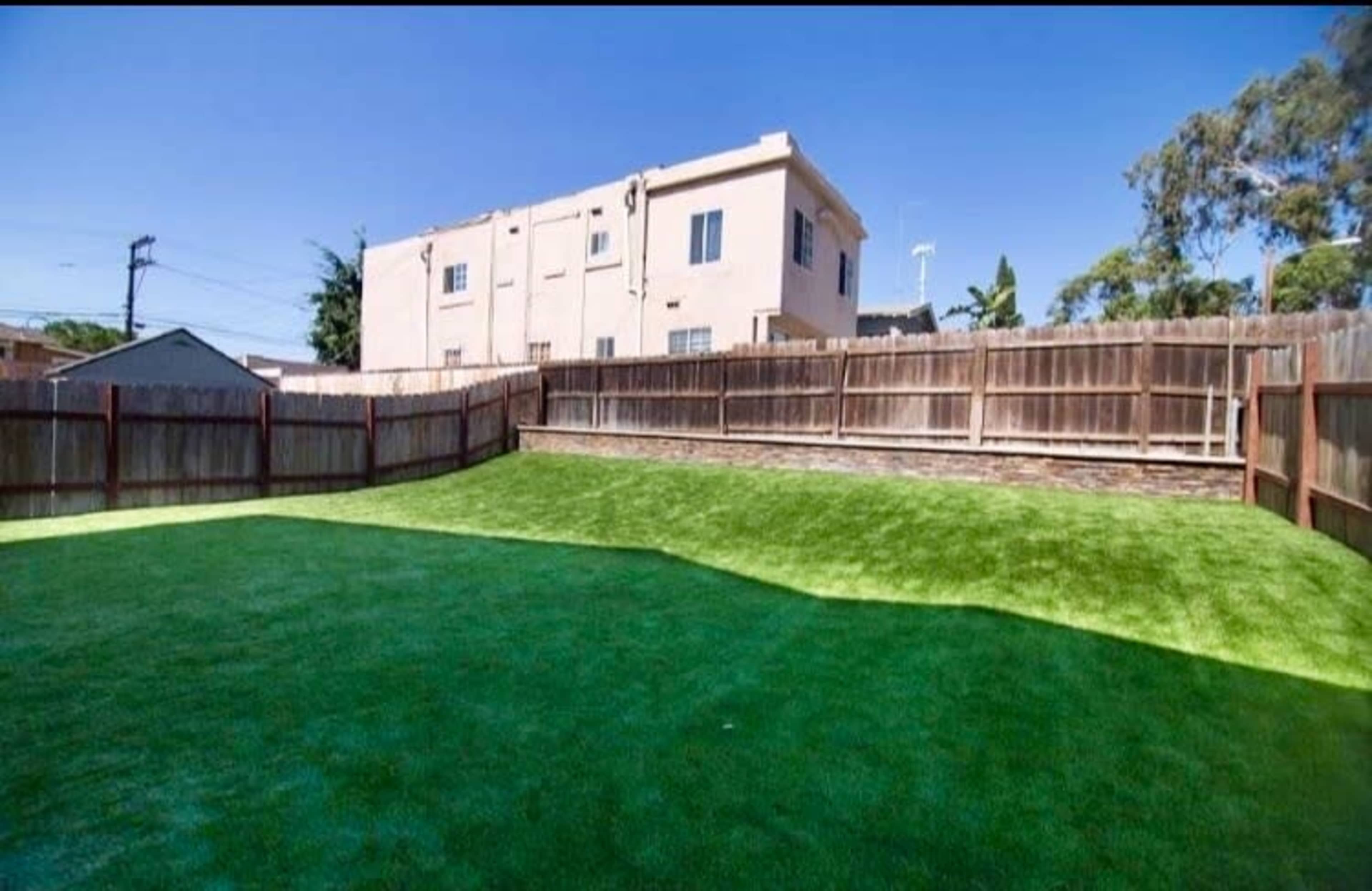 A fenced backyard featuring artificial turf and a building in the background.