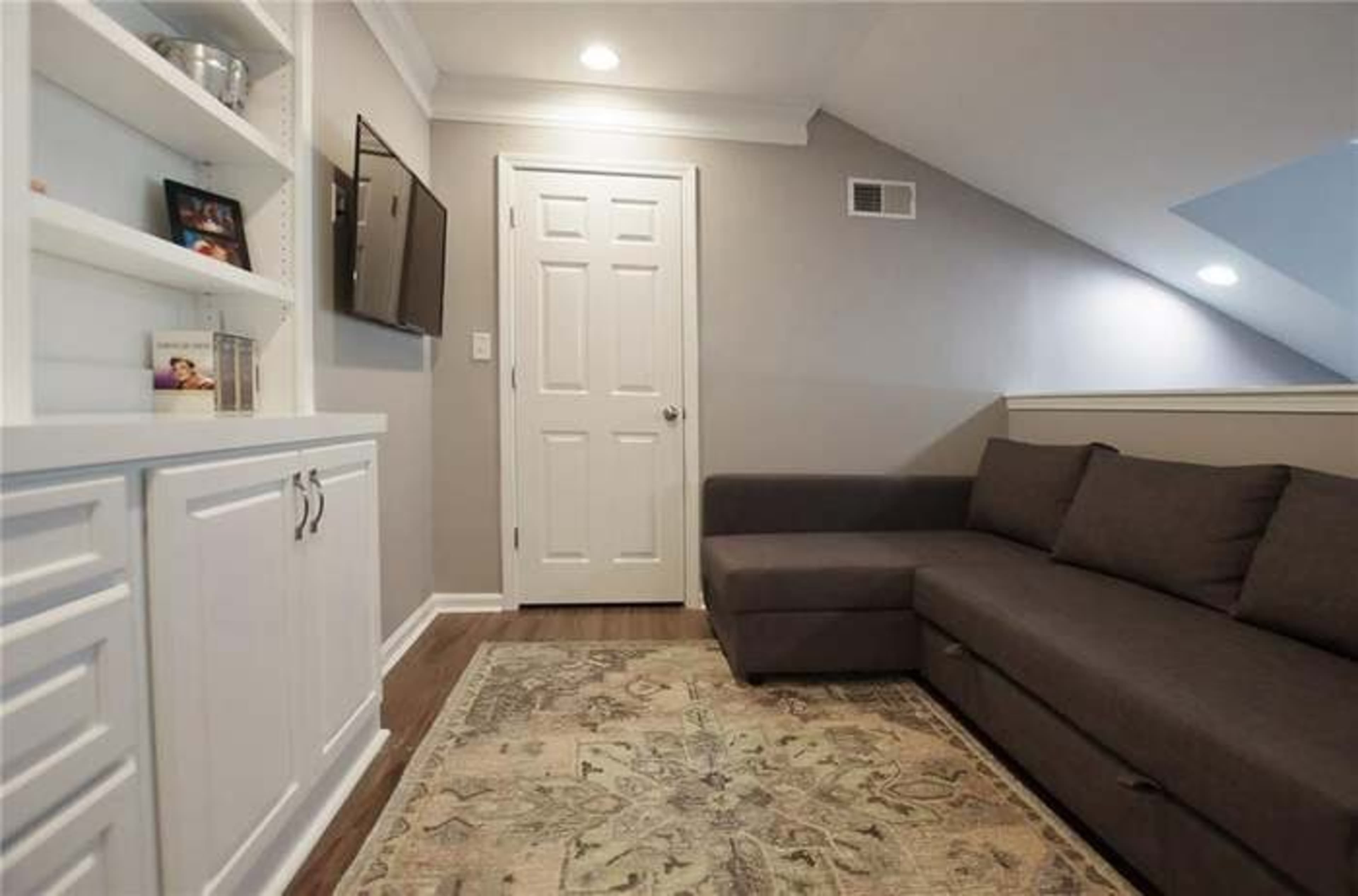 A cozy living space with a sectional sofa, a wall-mounted TV, and a white built-in shelf against the wall.
