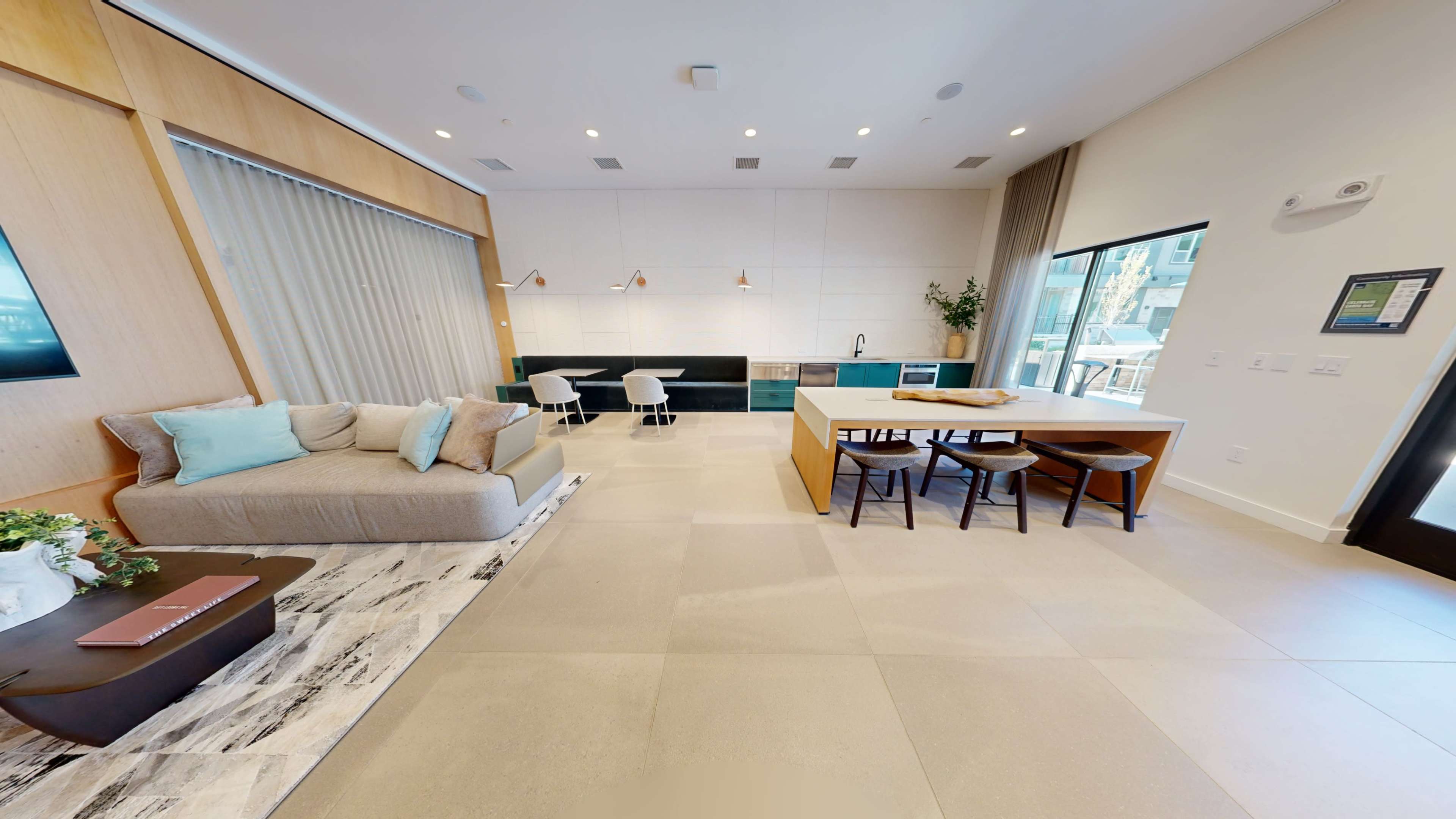 A modern open-concept living area featuring a sectional sofa, a dining table with chairs, and a kitchen with a large island and appliances.