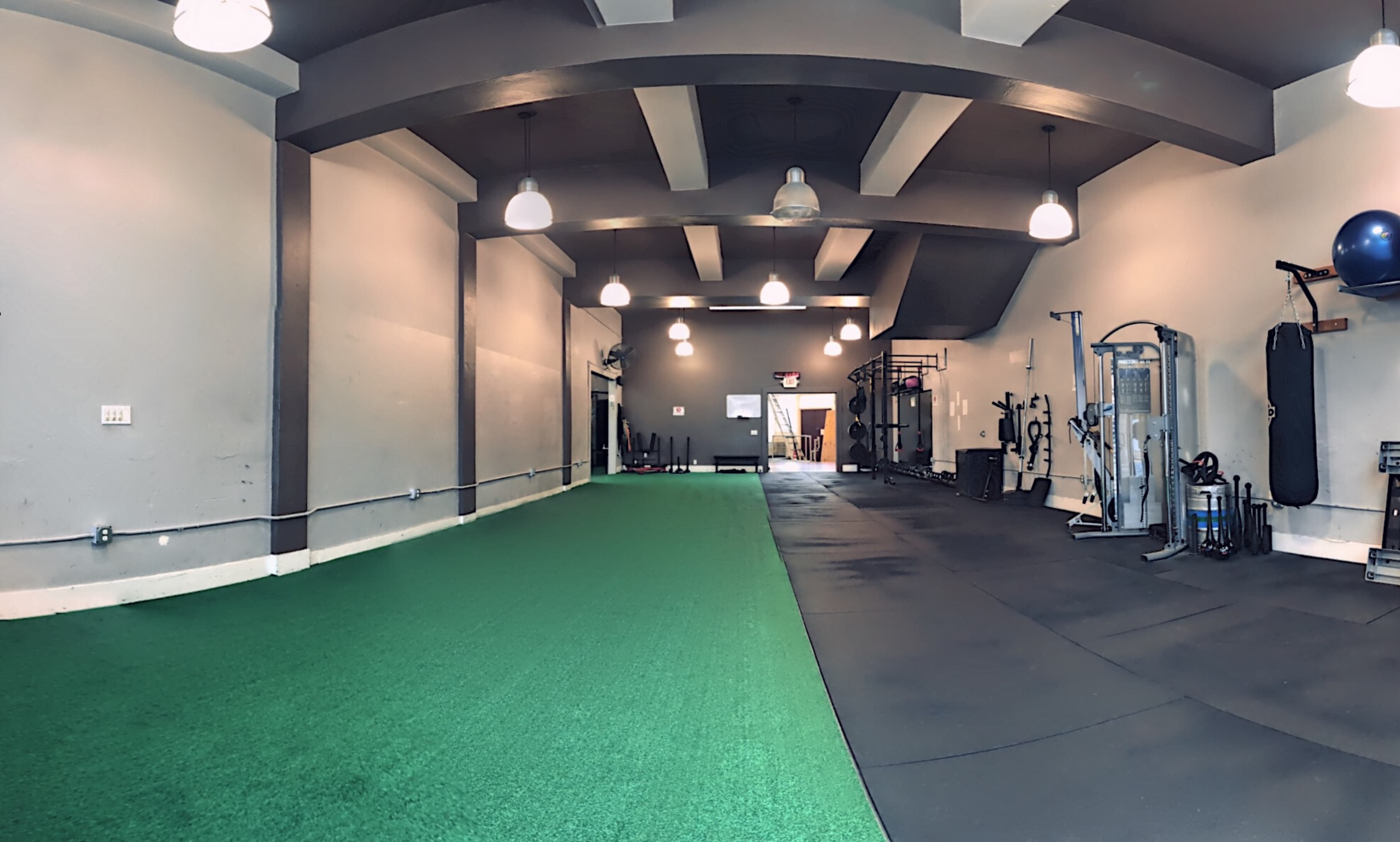 A spacious gym interior featuring a green artificial turf area on one side and rubber flooring with various workout equipment on the other.