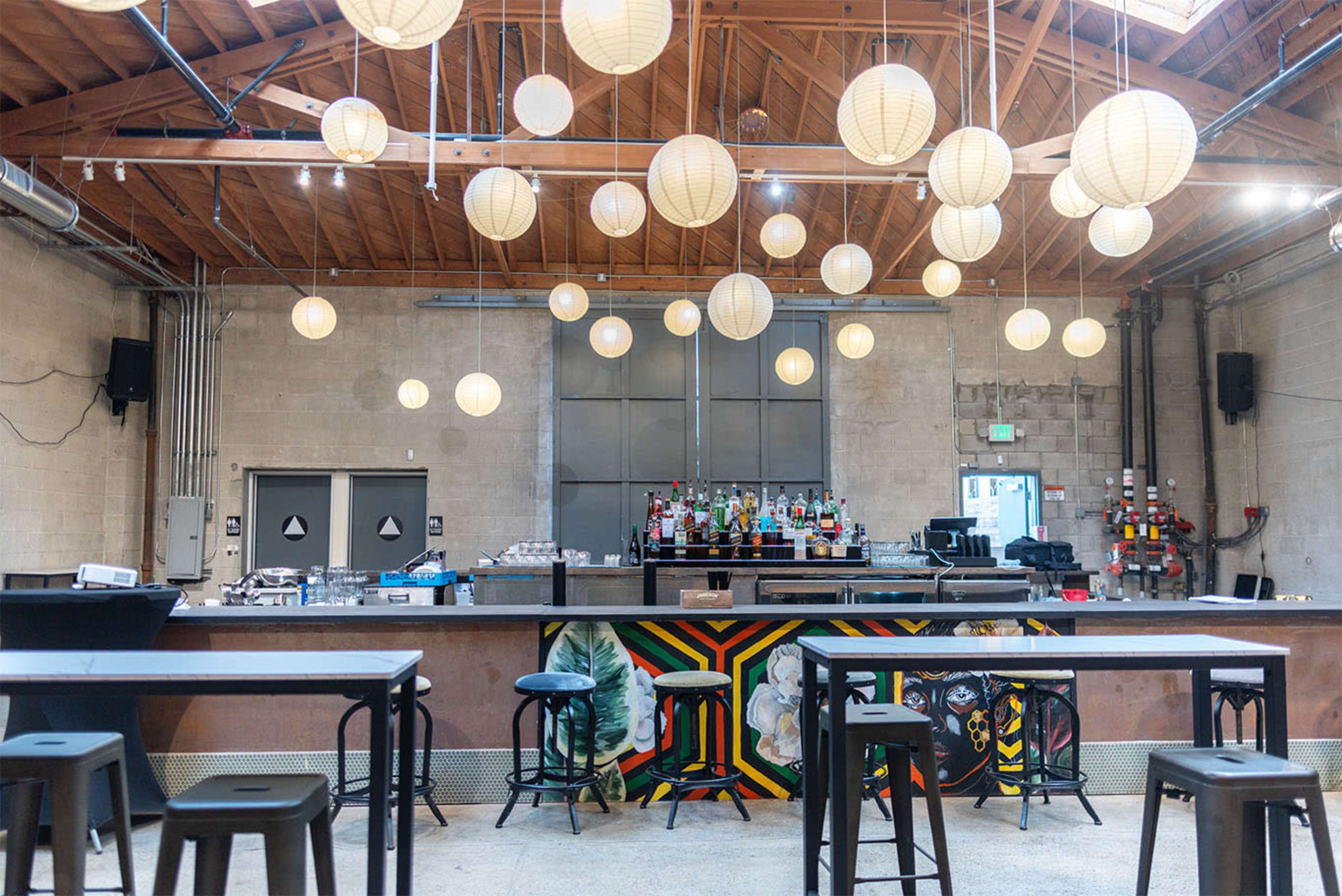 The image shows a modern bar with a wooden ceiling, string lights, and a decorative mural behind the counter.