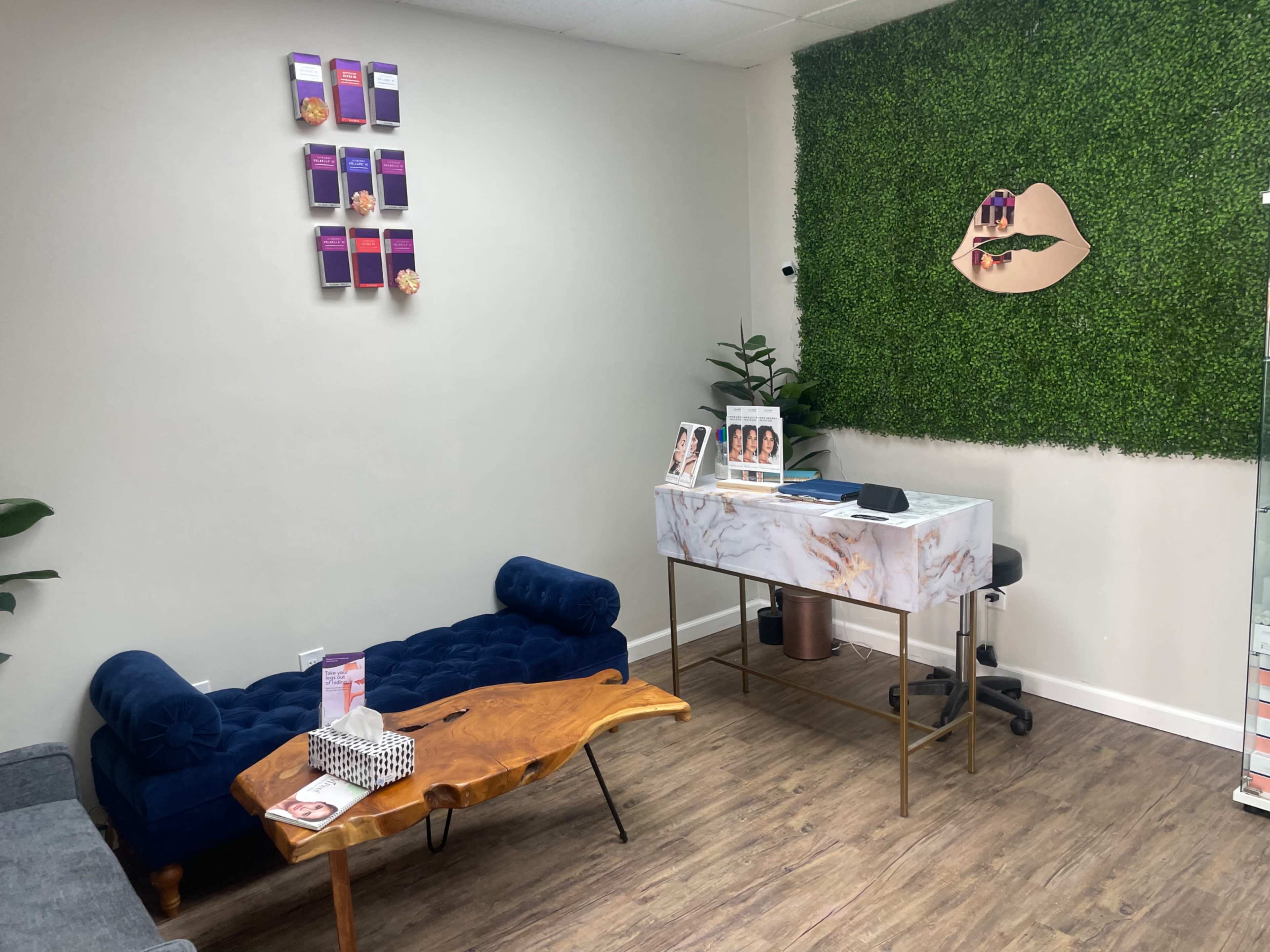 A stylish reception area with a blue velvet couch, a wooden coffee table, and a marble reception desk against a backdrop of green foliage.