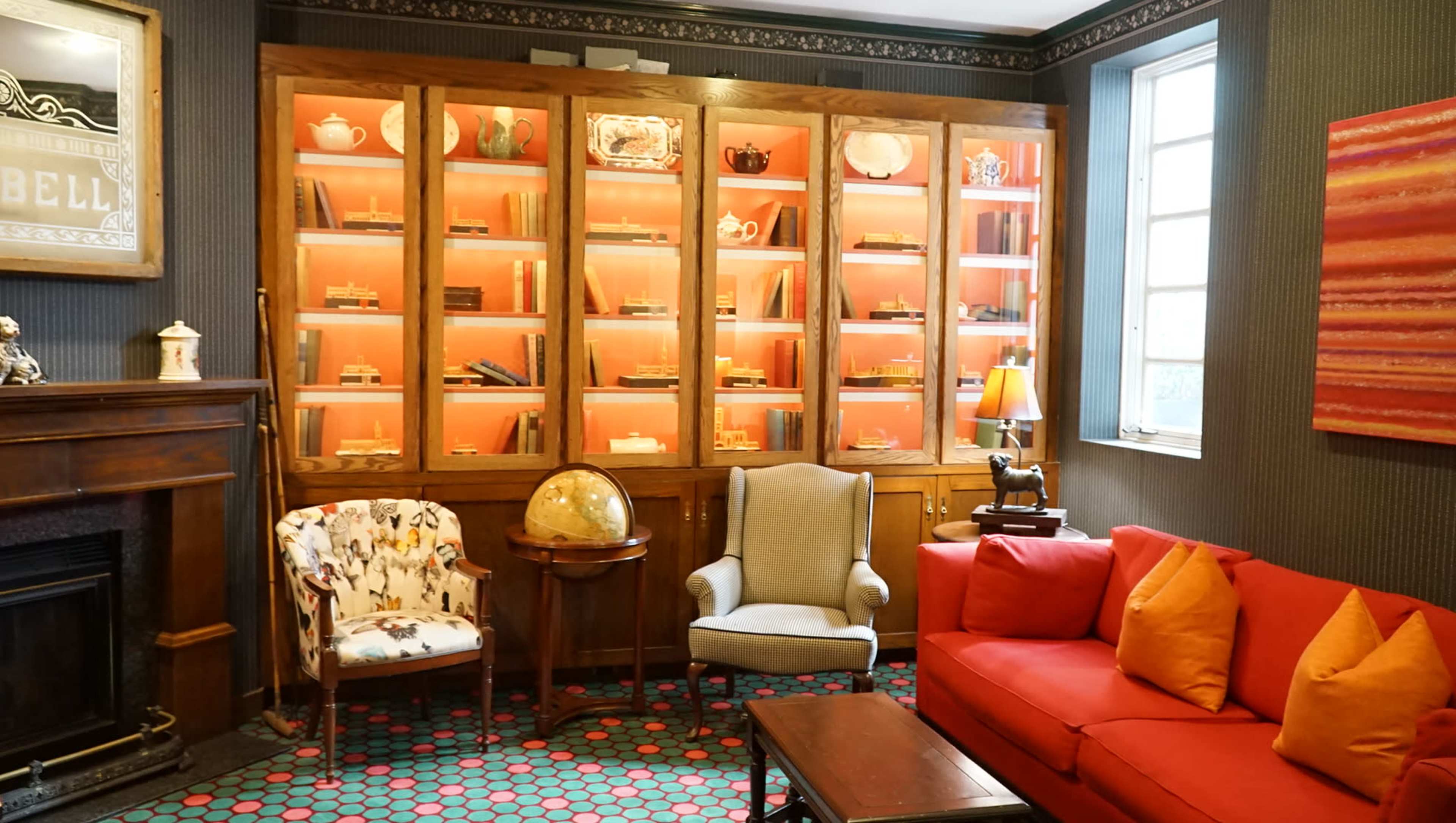 A cozy room with a red couch, two armchairs, and a display cabinet filled with items, illuminated by soft pink lighting.