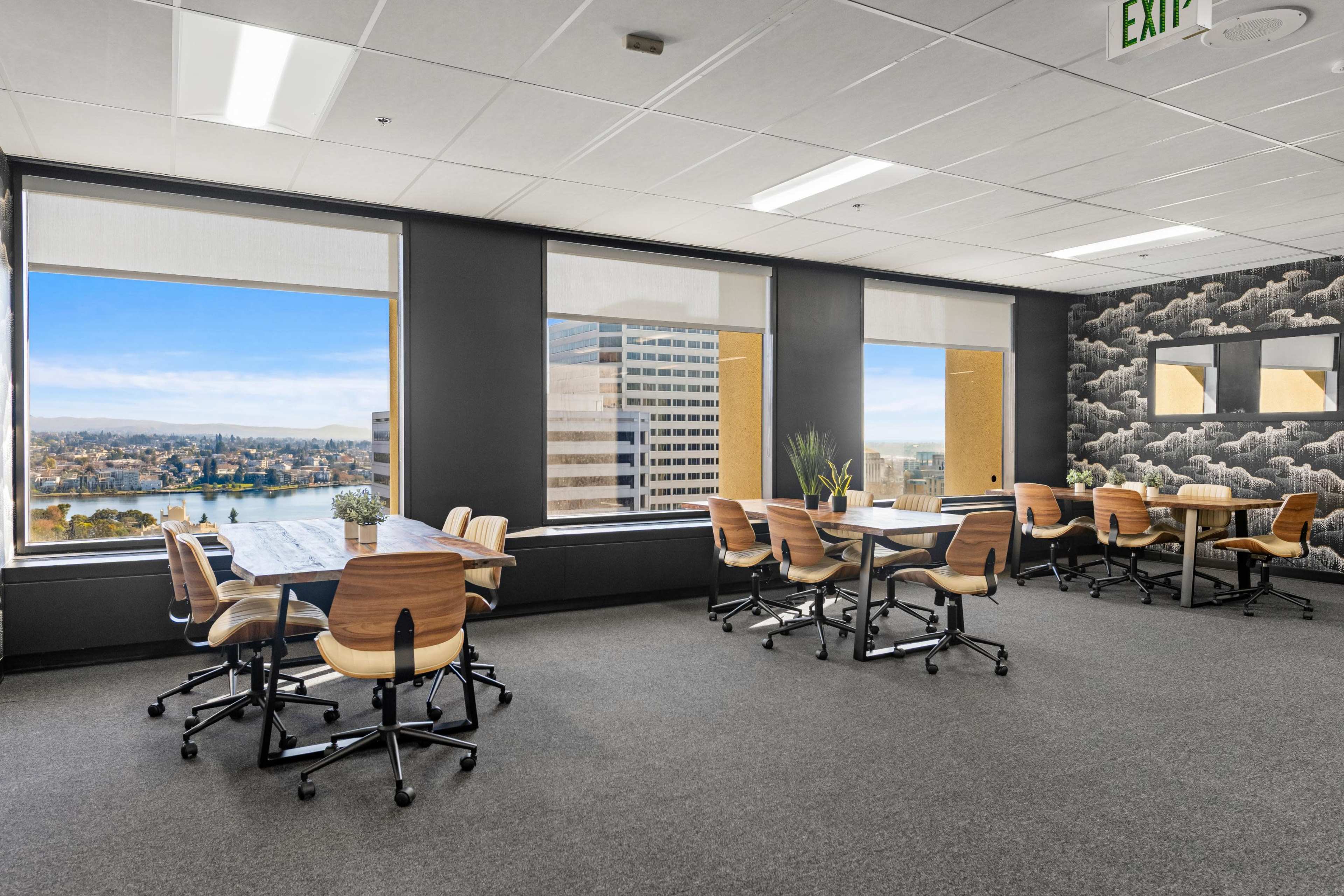 The image shows a modern office space with tables and chairs arranged for meetings, featuring large windows that offer a view of a cityscape.