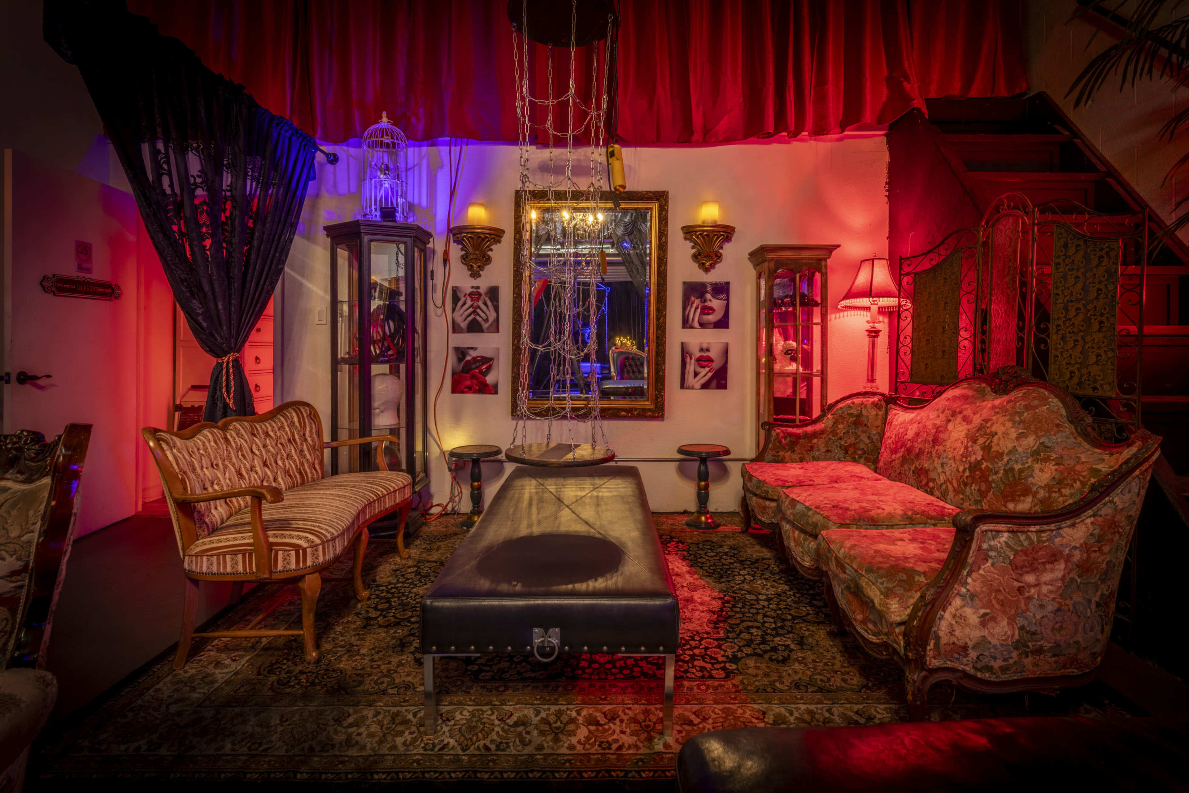 The image shows a dimly lit vintage-style parlor featuring ornate seating, a large mirror, and decorative elements illuminated by colorful lighting.