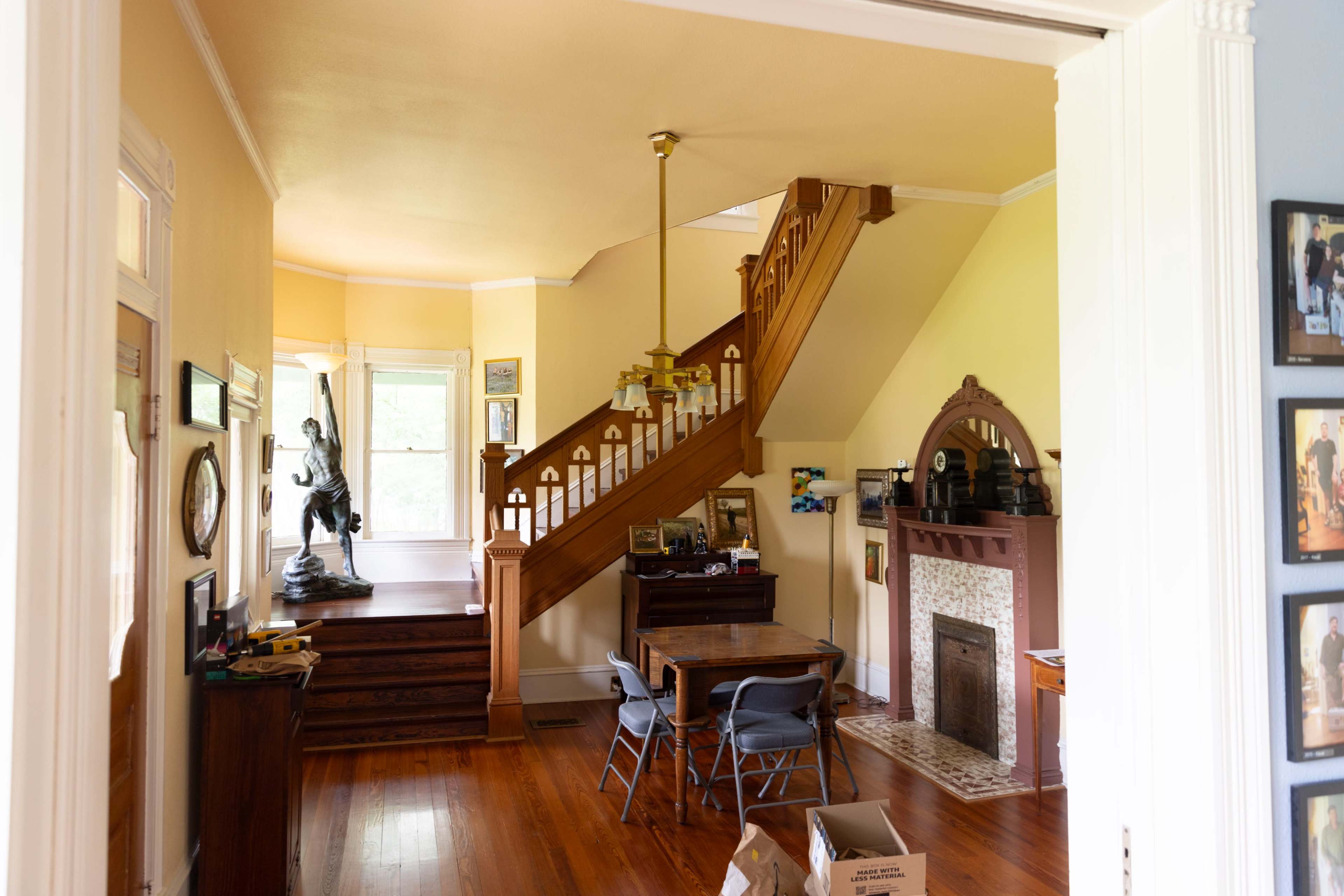 A bright room with a staircase, wooden furniture, and a small fireplace, leading to an open space with large windows.