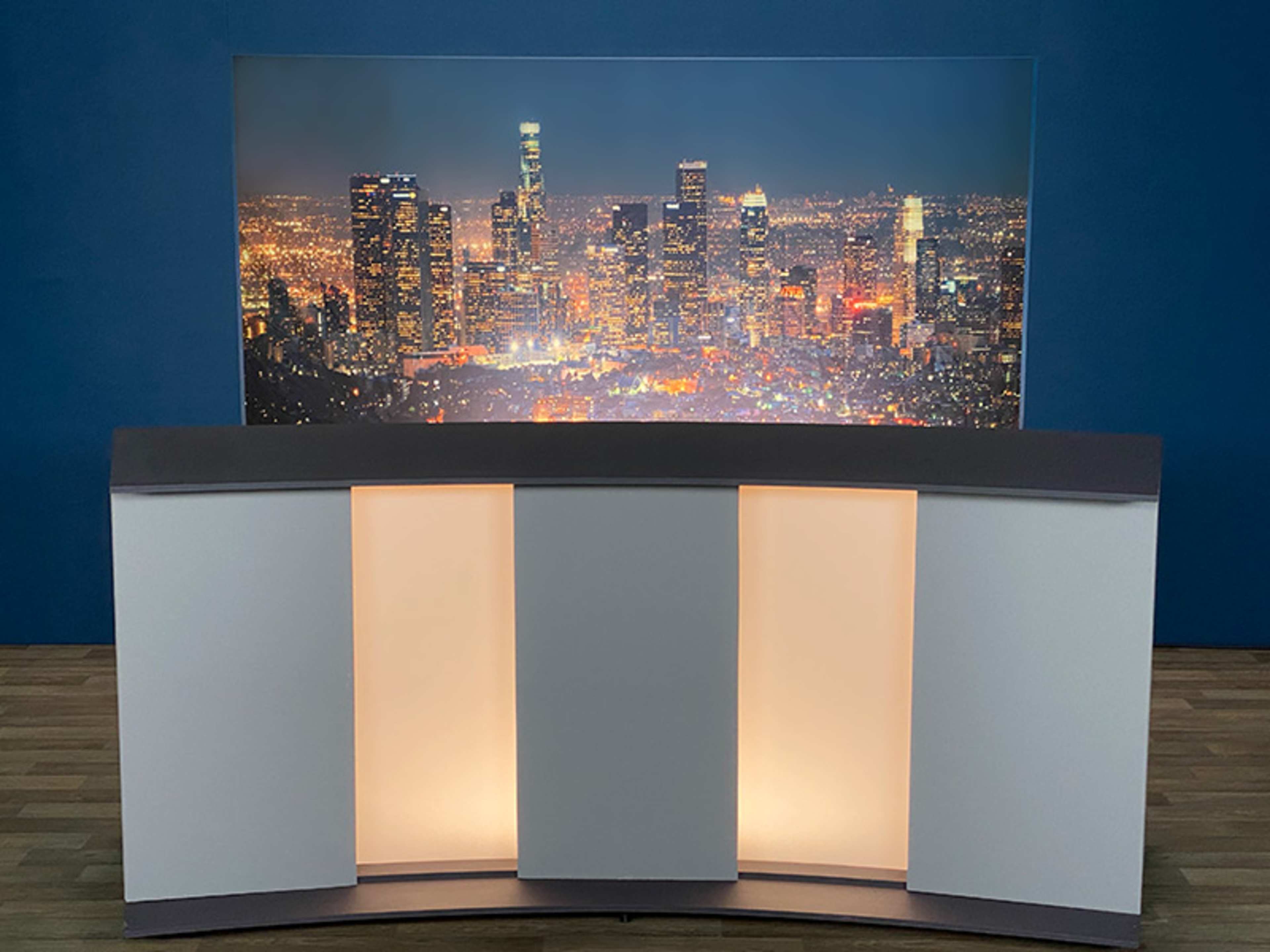 A modern broadcasting studio setup featuring a curved counter in front of a backdrop displaying a nighttime city skyline with bright lights.