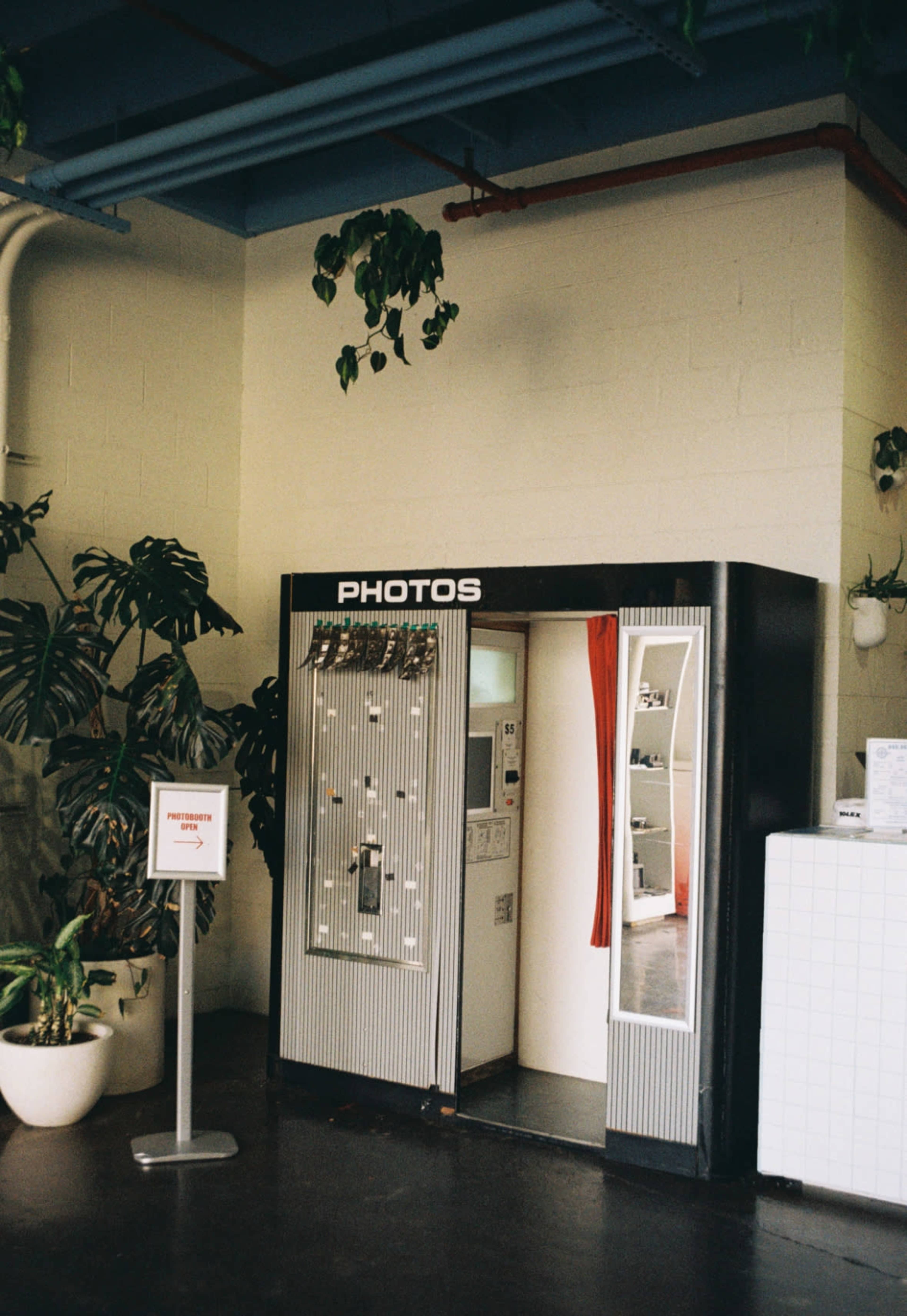 A vintage photo booth is situated in a corner of a room adorned with potted plants.