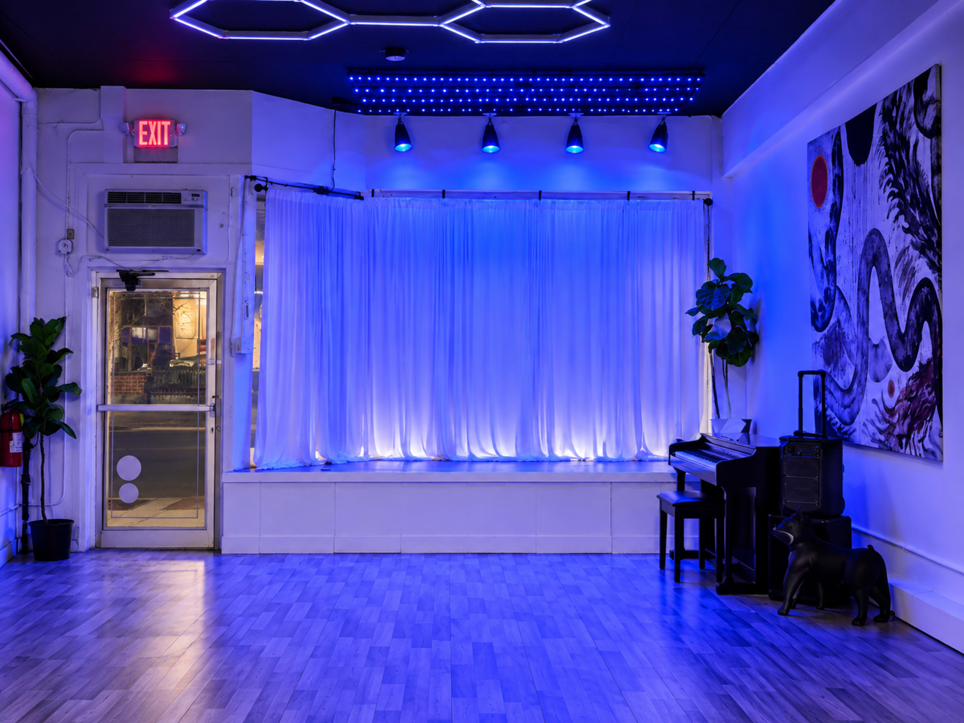 The image shows an indoor space featuring blue lighting, a curtain backdrop, a piano, a decorative plant, and an abstract wall painting.