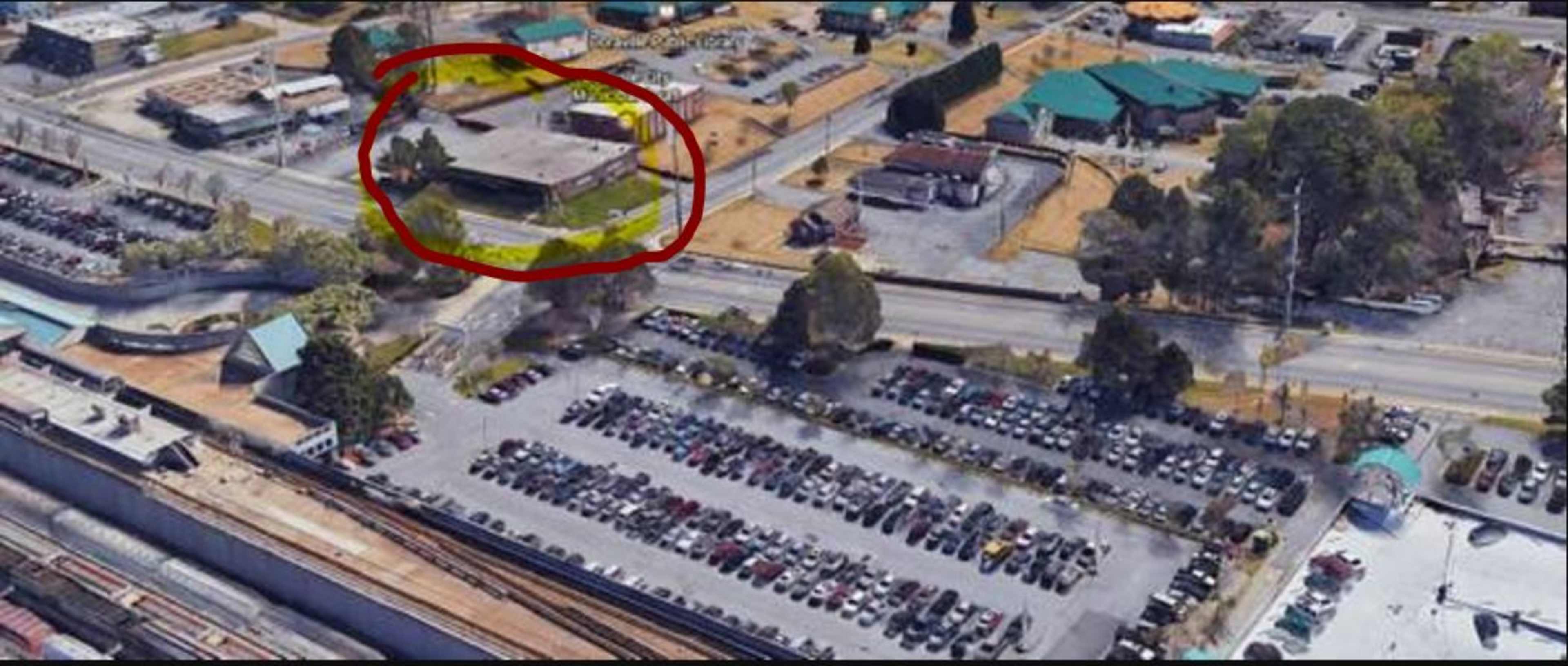 An aerial view of a parking lot with numerous cars, surrounded by several commercial buildings and roads.
